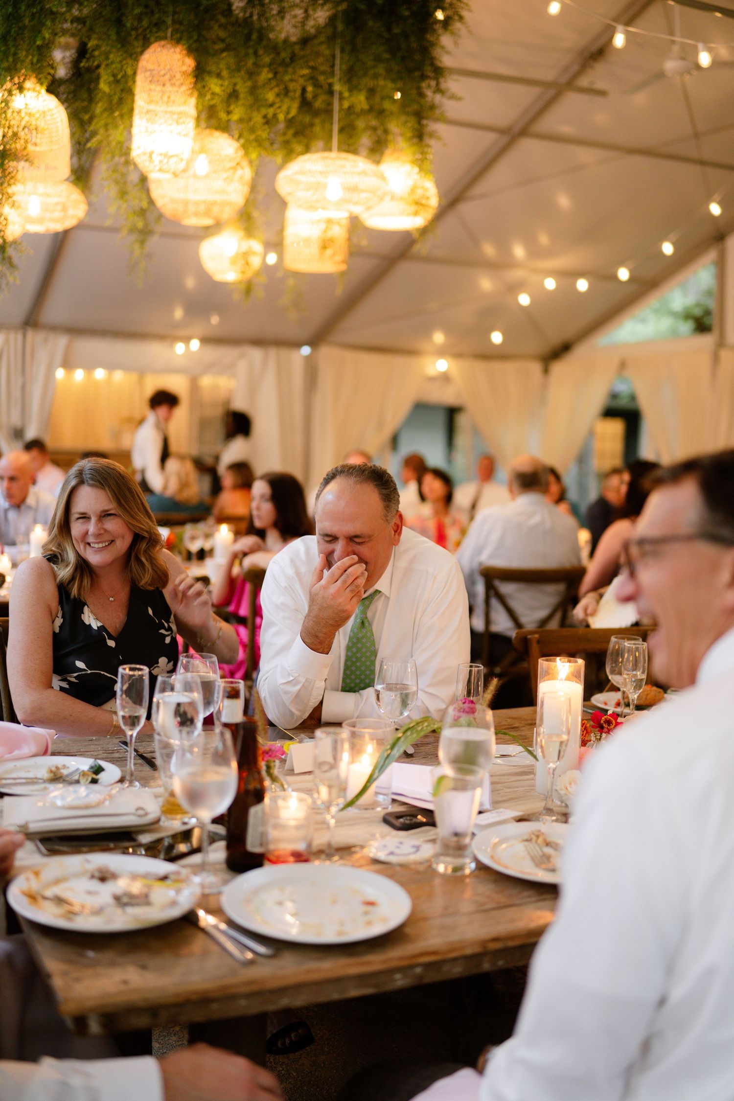 Wedding reception dinner under a tent with elegant lighting and table settings.