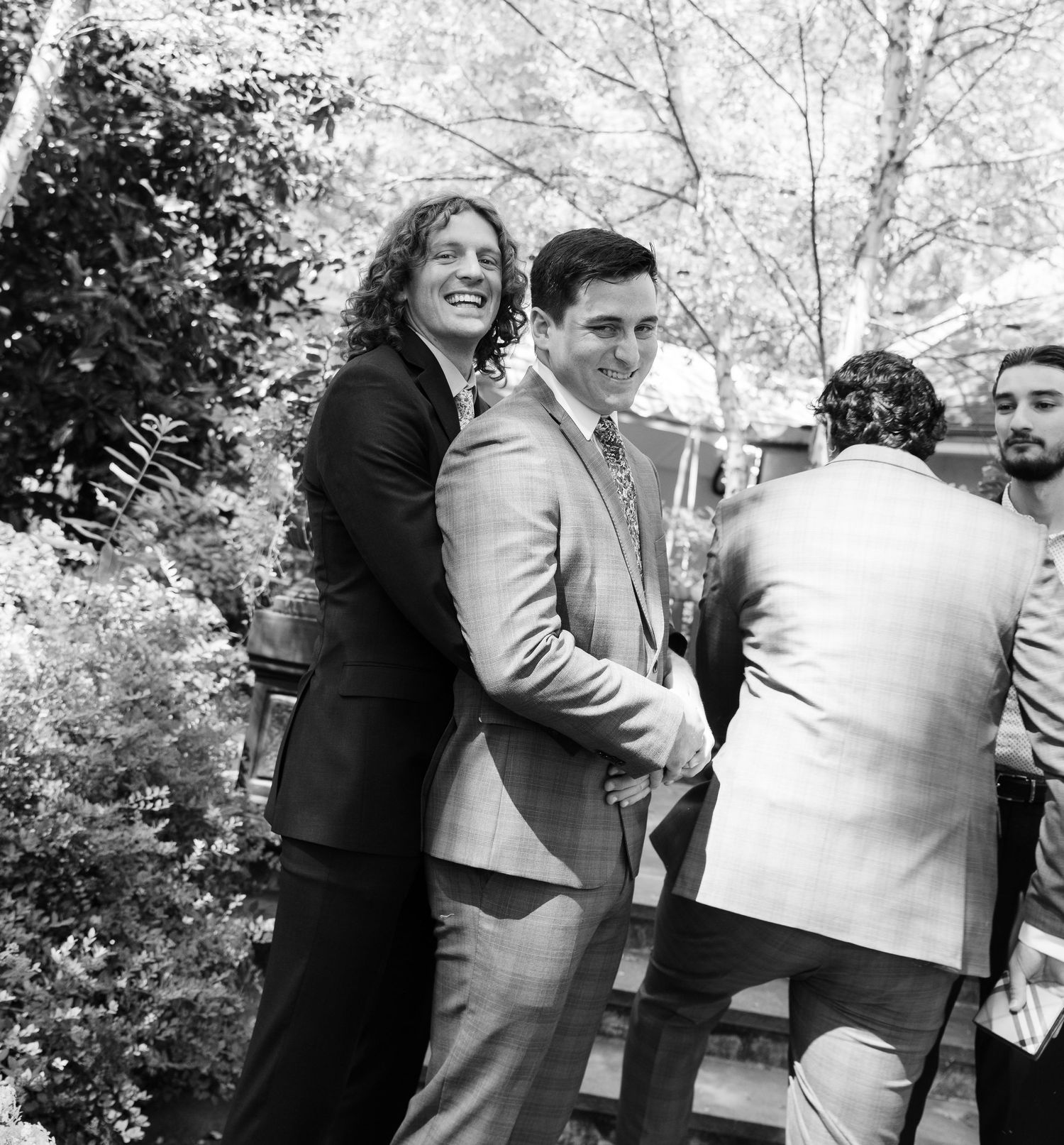 Black and white photo of wedding guests embracing and celebrating outdoors.