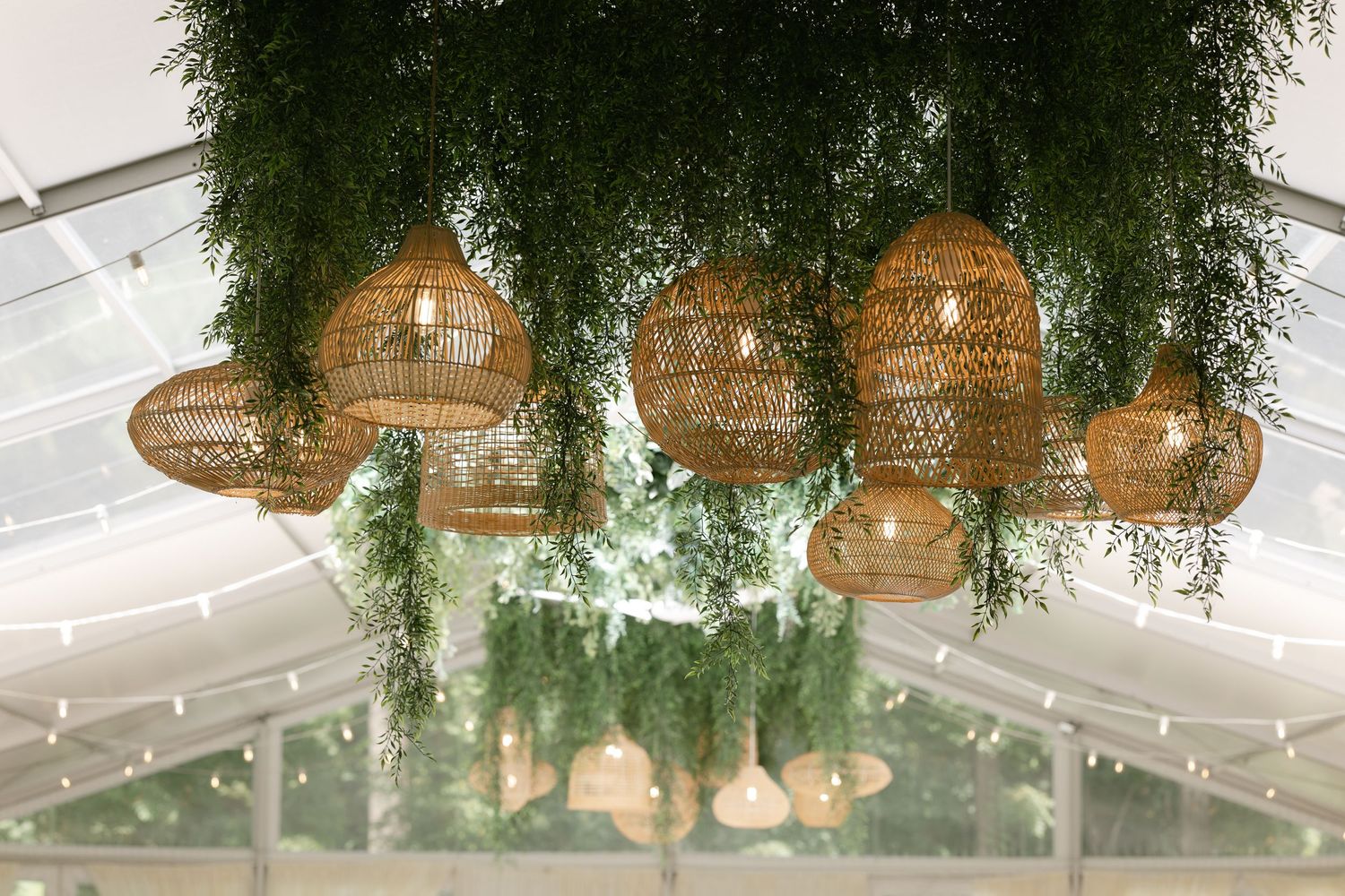 Woven rattan pendant lights hang from a white ceiling with cascading greenery creating a tropical bohemian atmosphere.