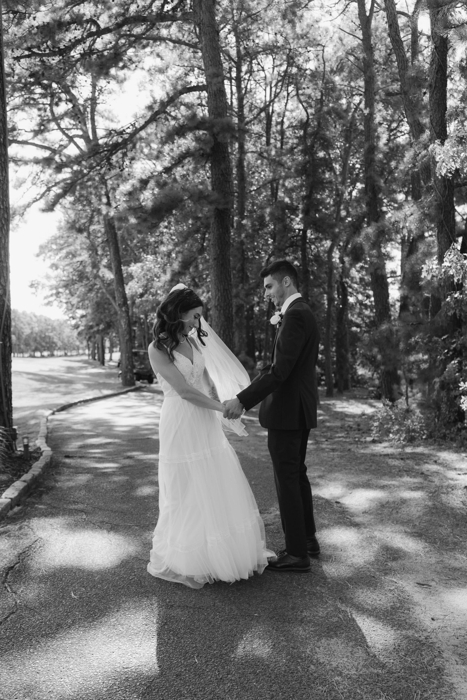 Black and white wedding photos showing a couple dancing together on a tree-lined path in a romantic outdoor setting.