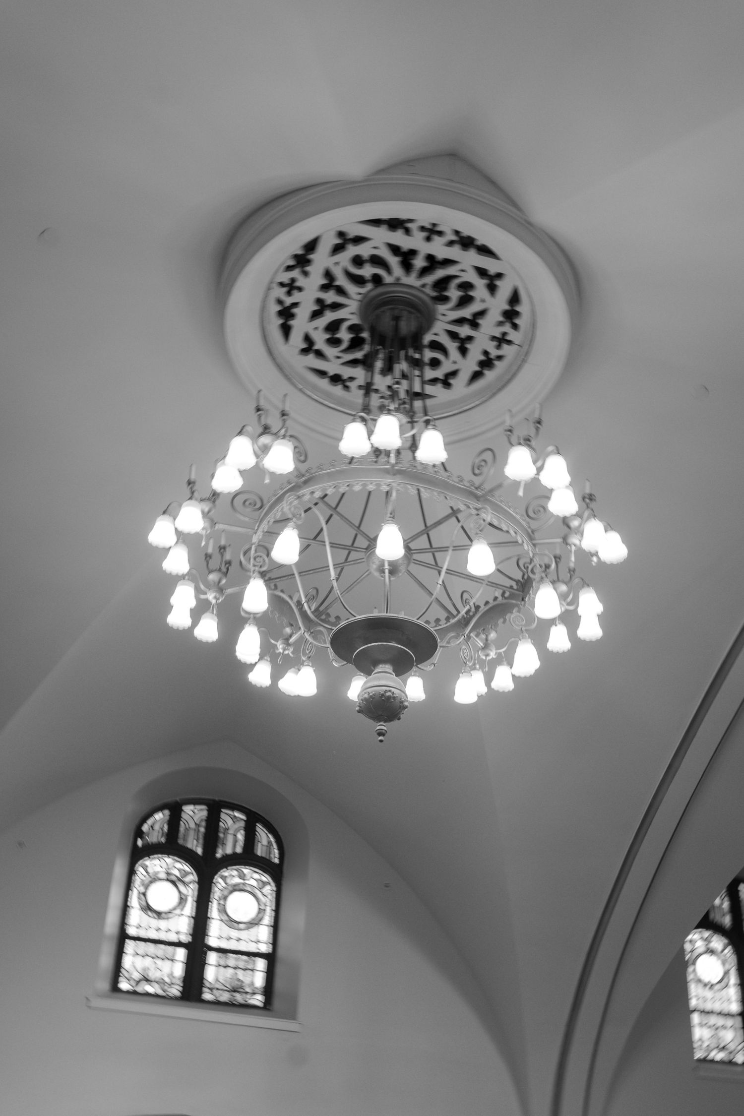 Elegant chandelier lights and stained glass windows adorn the vaulted ceiling of a historic venue.