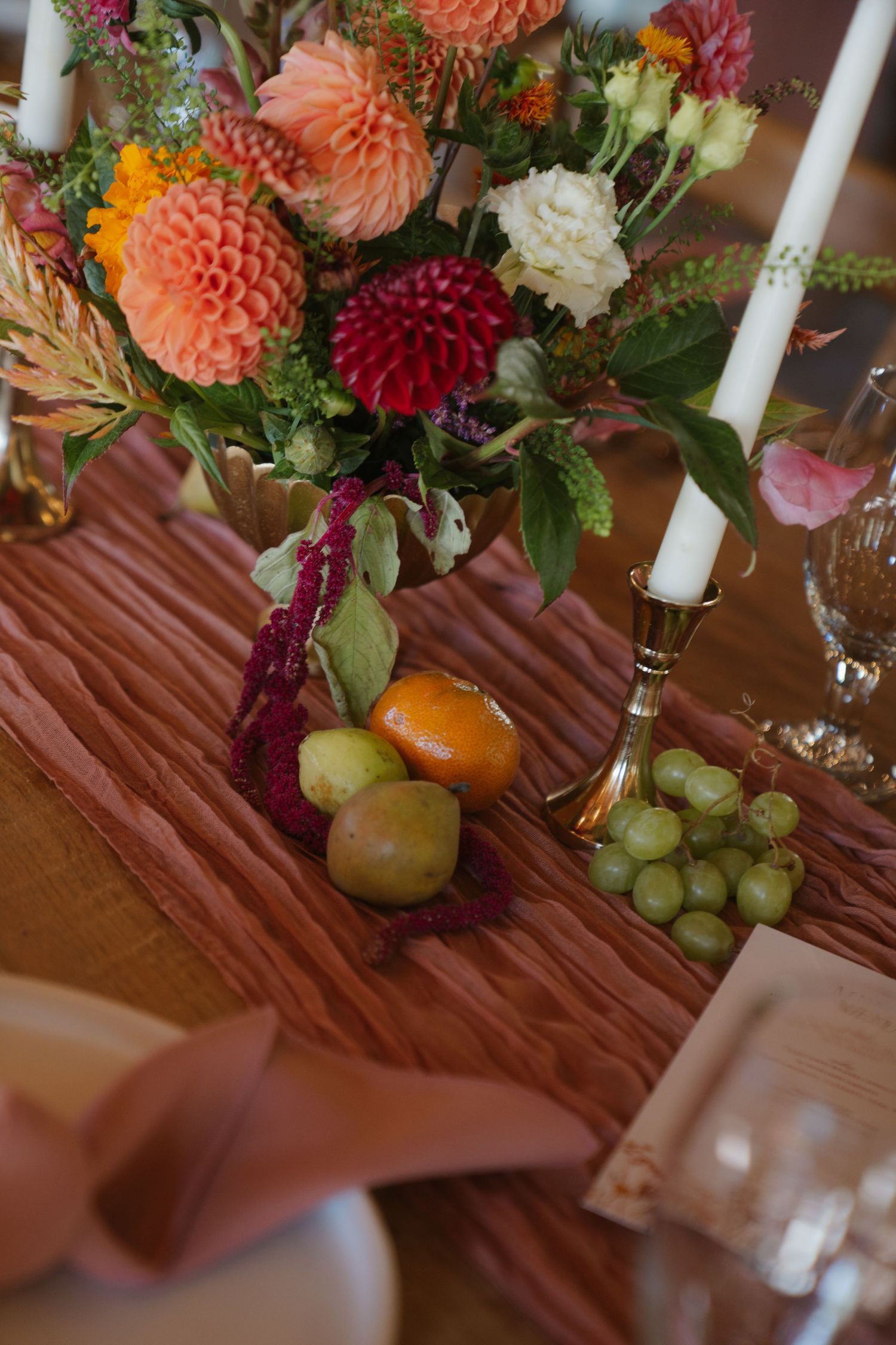 Elegant table decor with colorful dahlias, fruit, and candles for wedding reception.