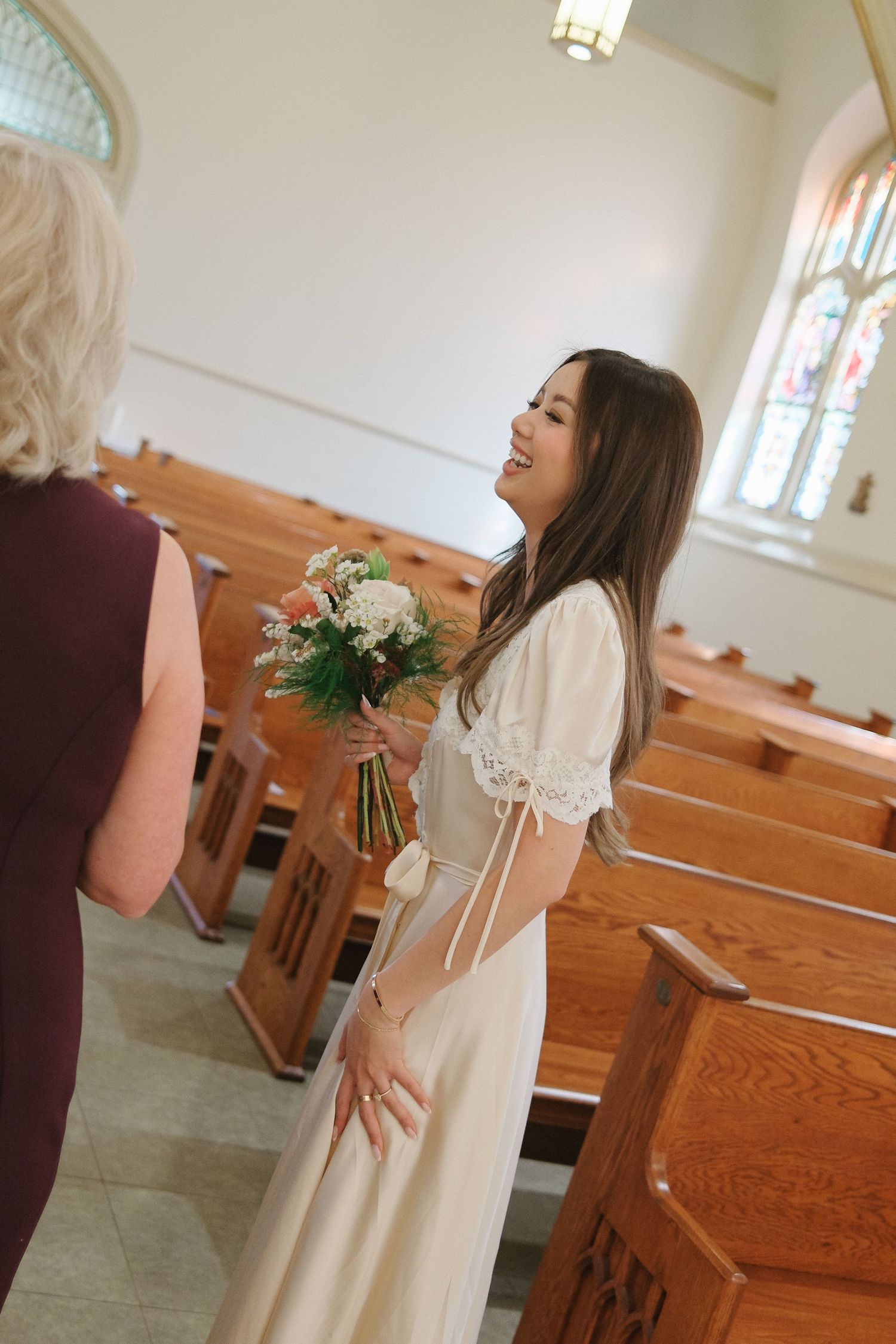 A joyful moment captured in a church with wooden pews and stained glass windows as a bride holds a floral bouquet.