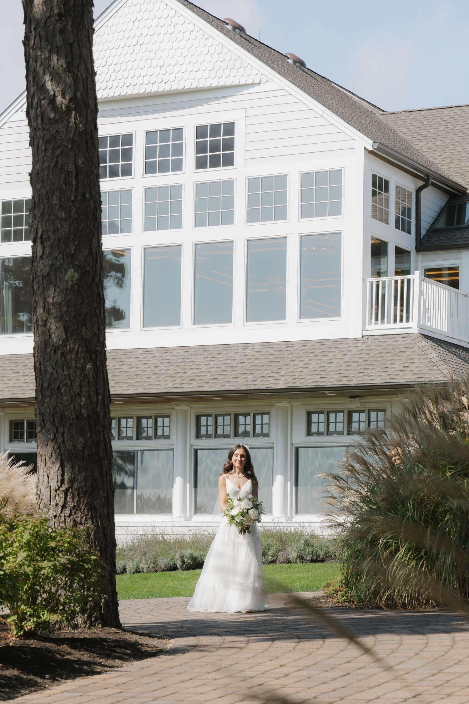 White wedding venue with large windows and a stone path leading to the entrance, surrounded by landscaped grounds.