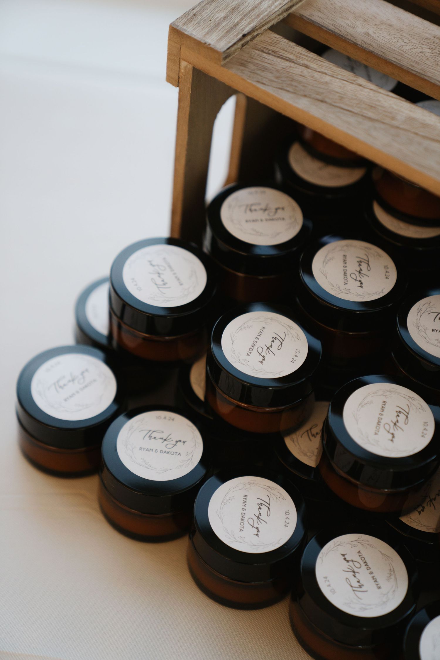 Small amber glass jars with white labeled lids arranged in rows inside a wooden crate.