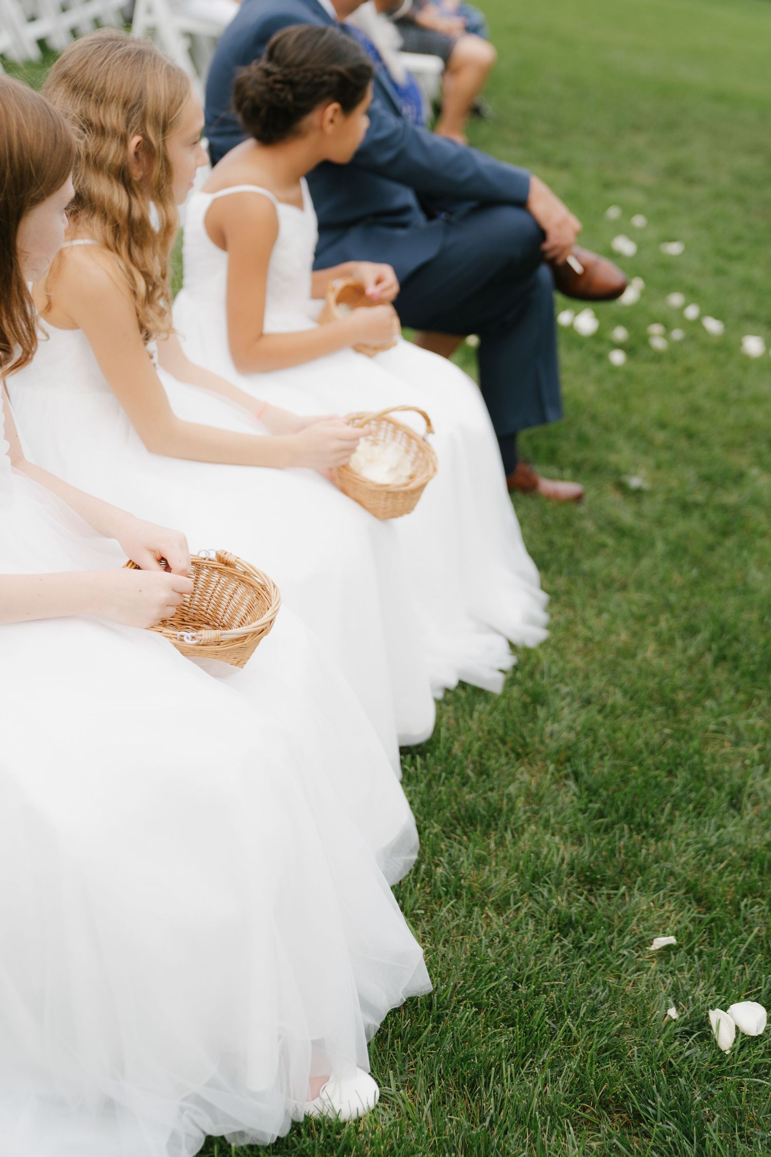 Wedding guests in formal attire sit on grass during an outdoor reception celebration.