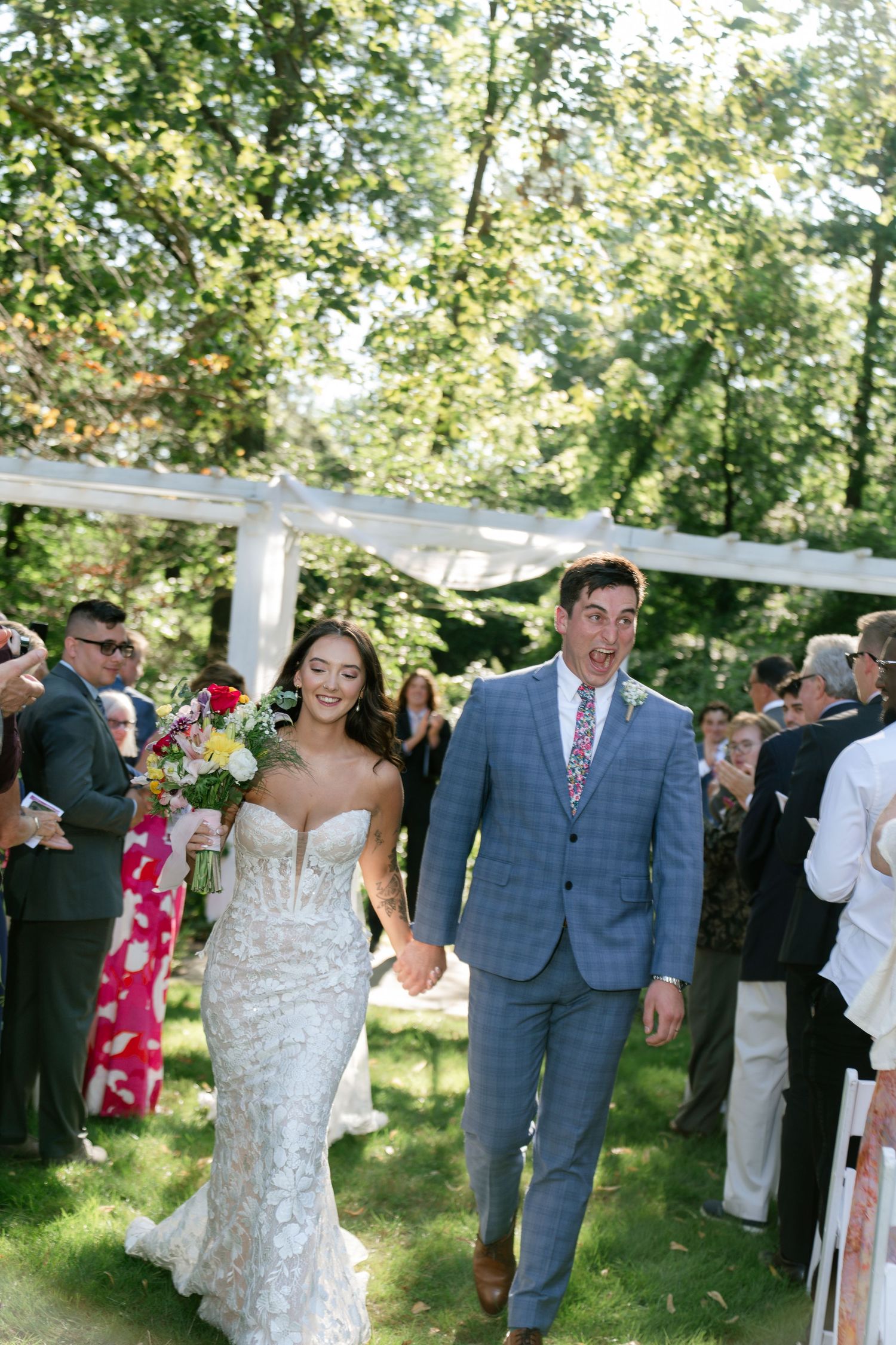 Wedding party walks under white canopy decorations in an outdoor garden ceremony setting.