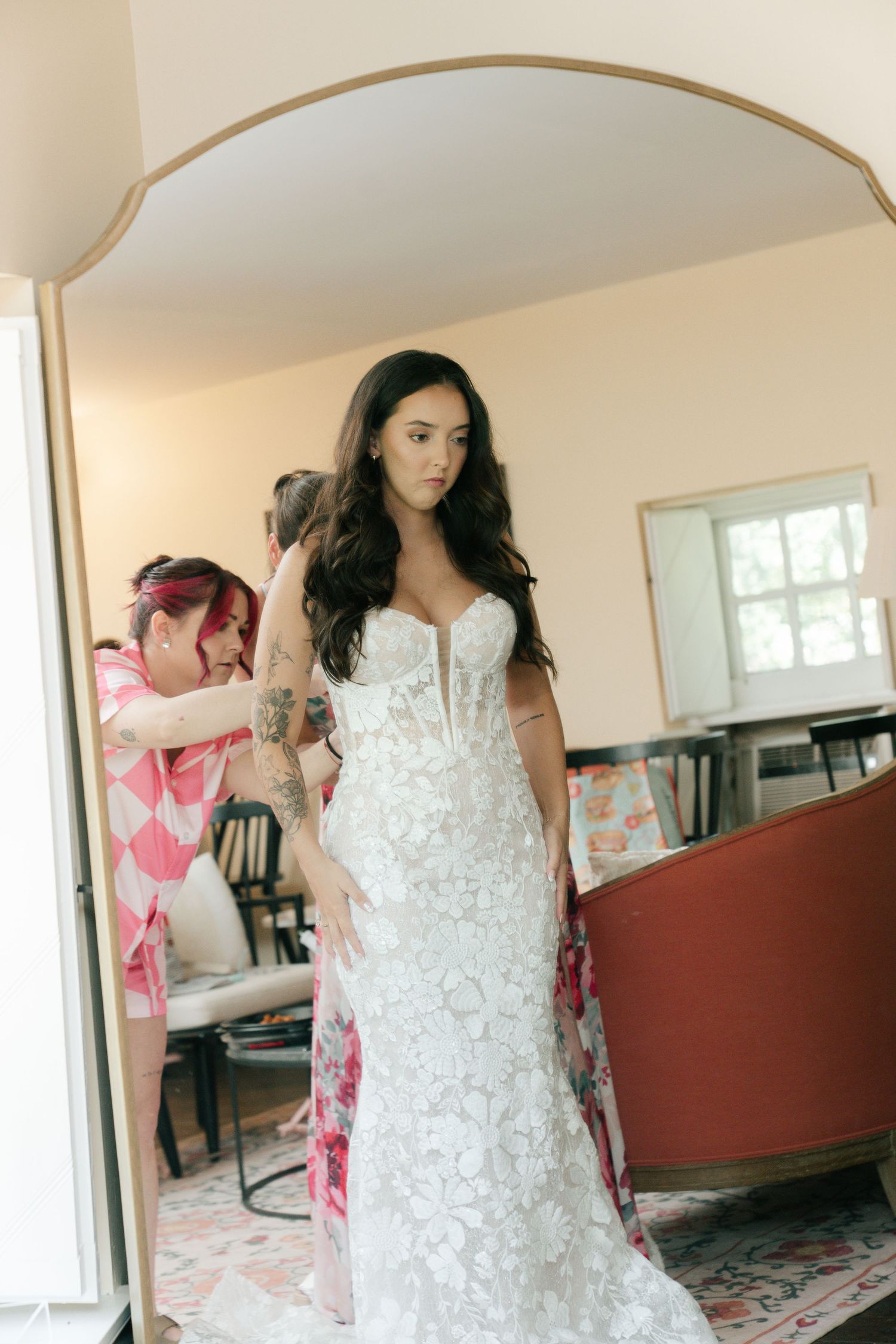 A beautiful white lace wedding dress being fitted in a sunlit room.