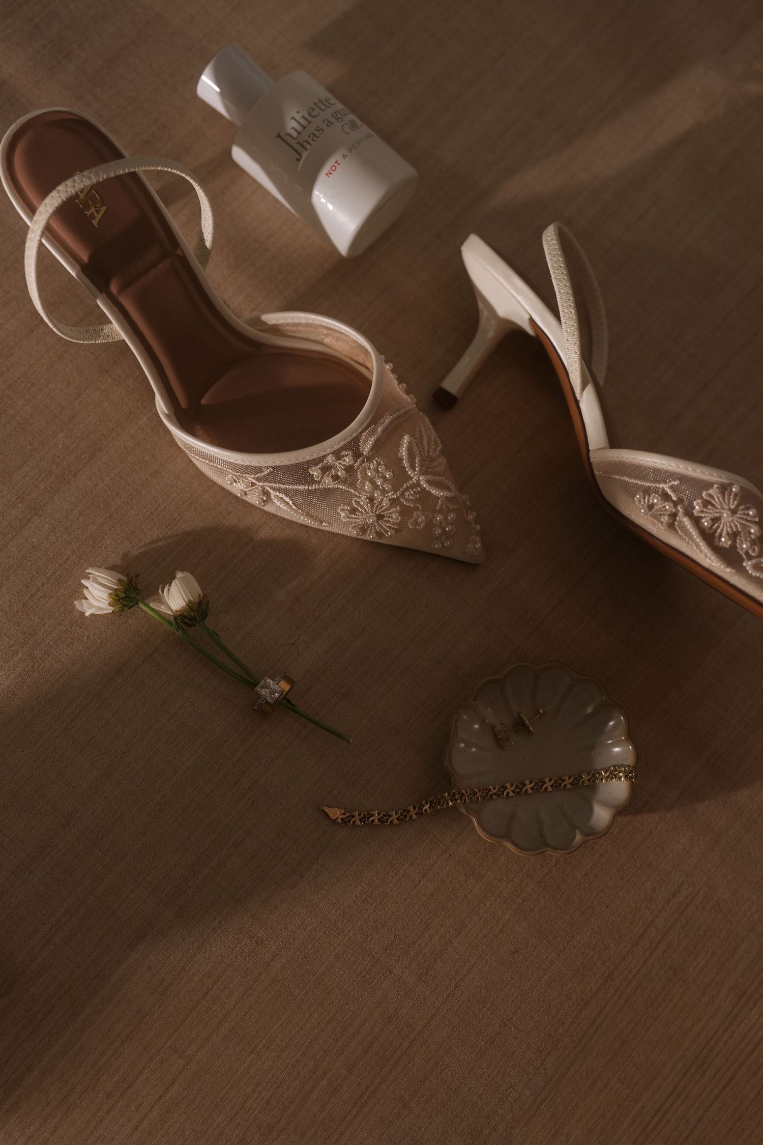 Wedding shoes and accessories arranged artistically on a wooden surface in warm, moody lighting.