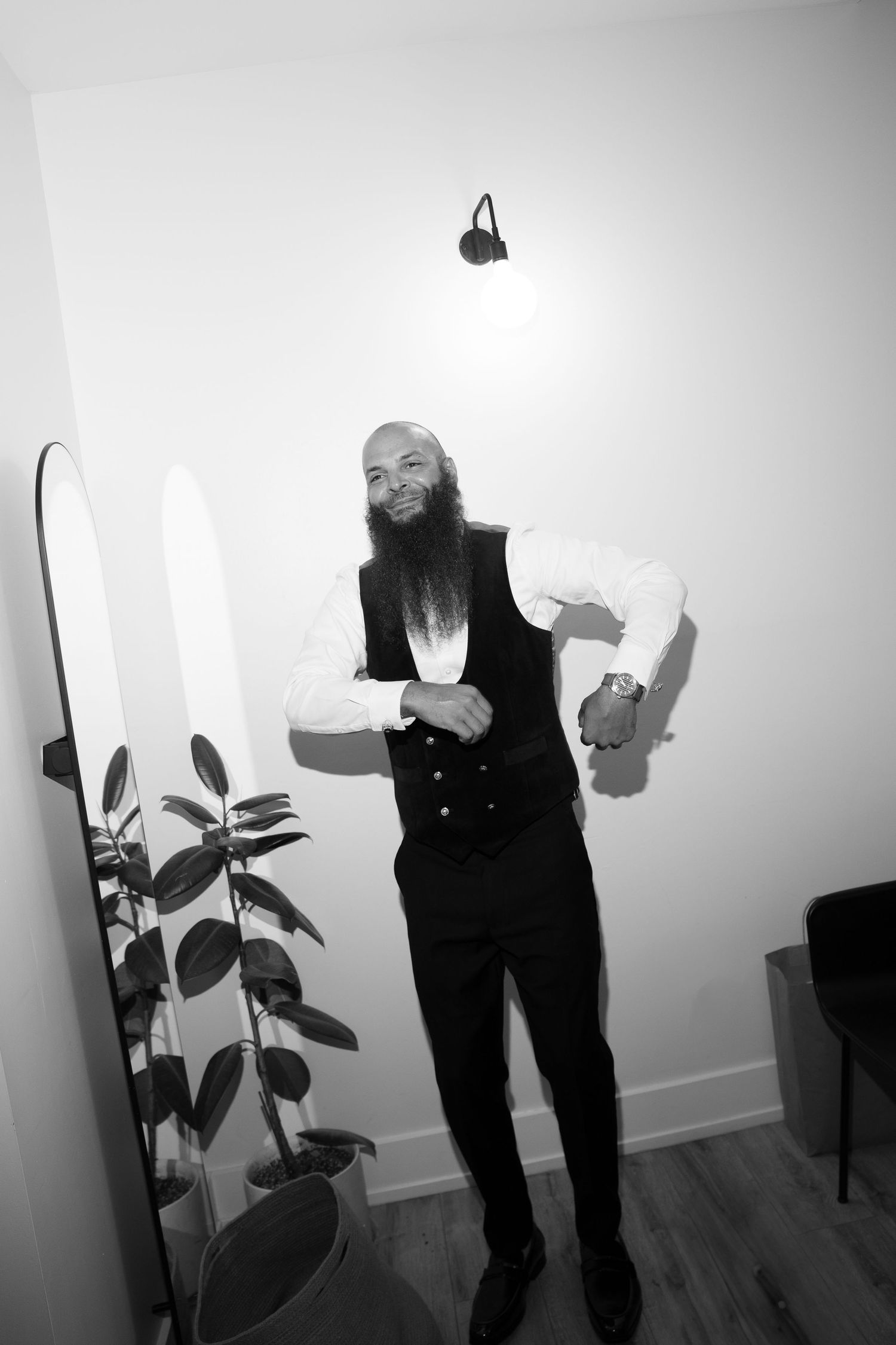 Black and white photo of a person in formal wear gesturing expressively against a white wall.
