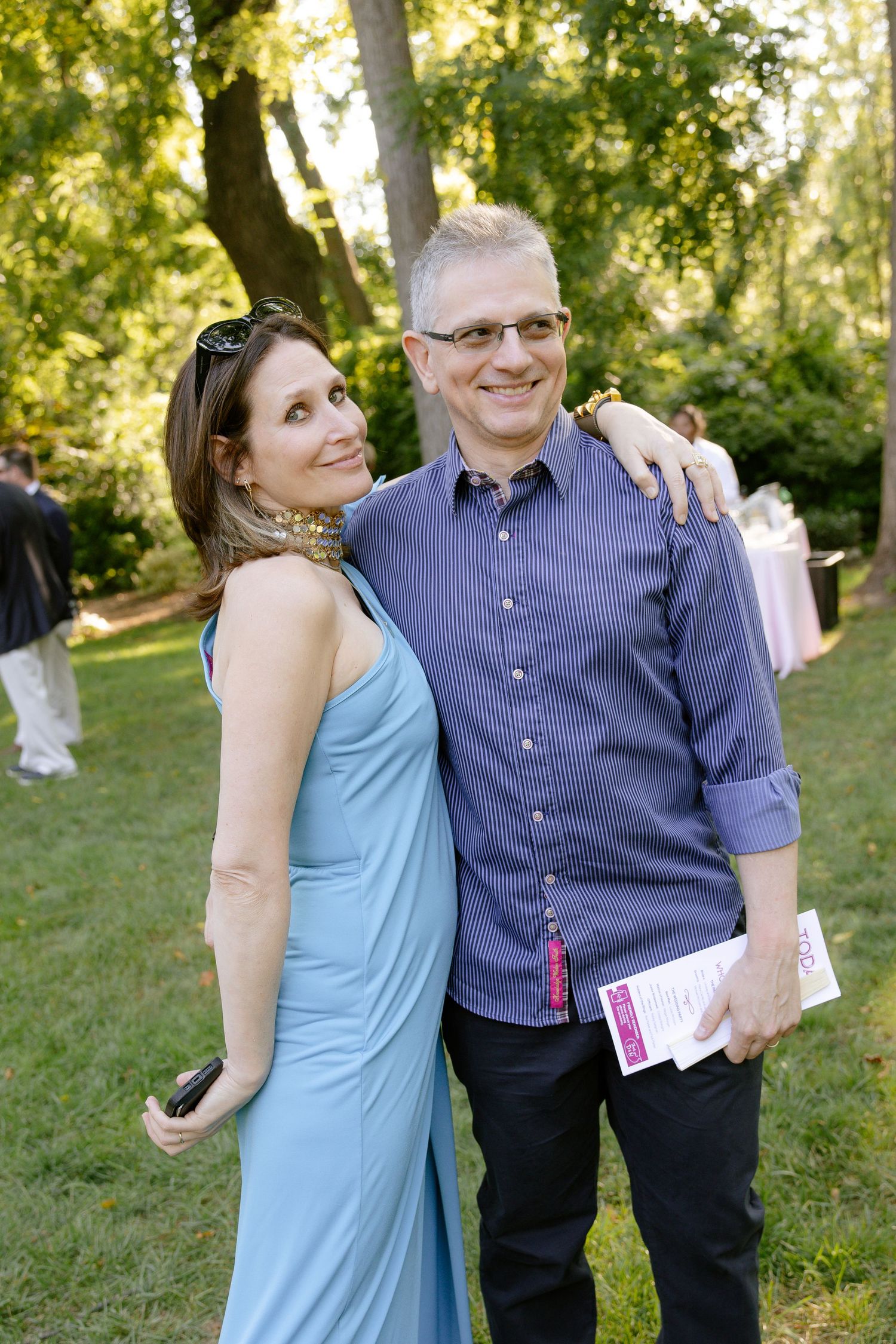 A couple poses together outdoors at a wedding celebration on a sunny day.