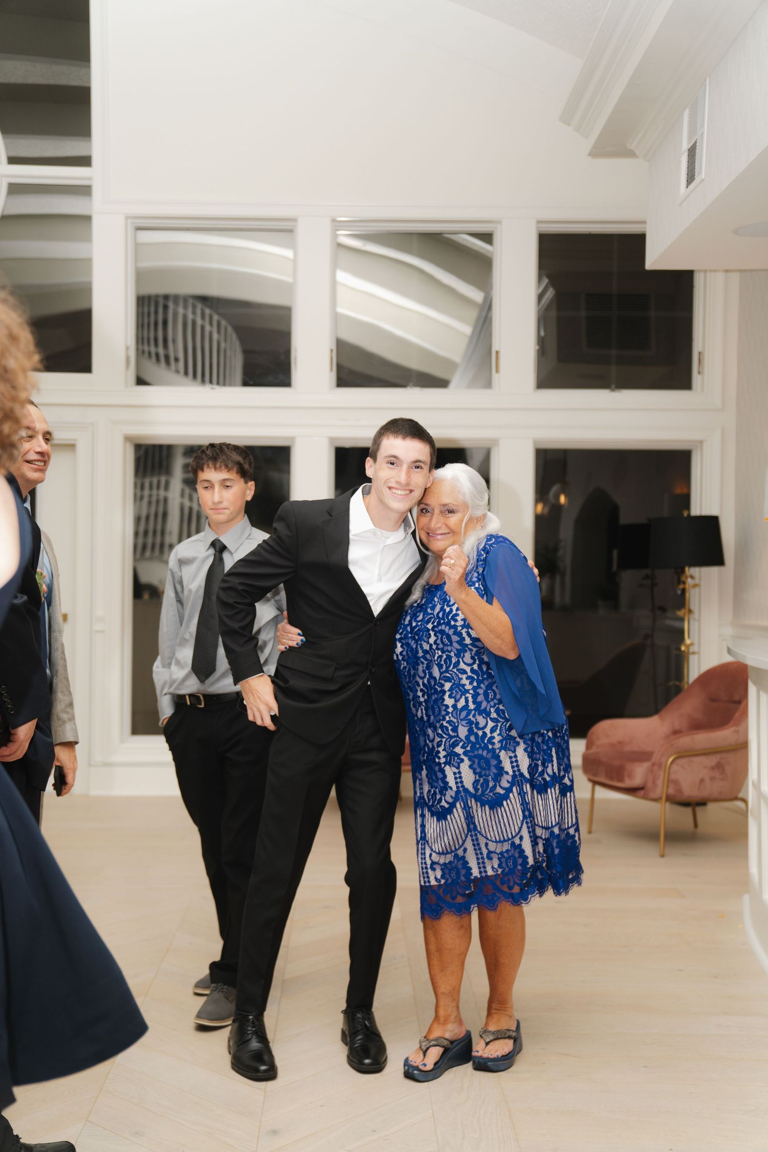 People in formal attire dance and interact in a bright white modern space with high ceilings and minimalist decor.