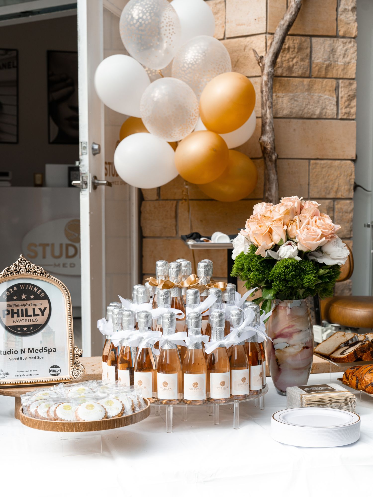 Elegant dessert table display with white and gold balloons, tiered stands, and delicate party favors for a celebration.
