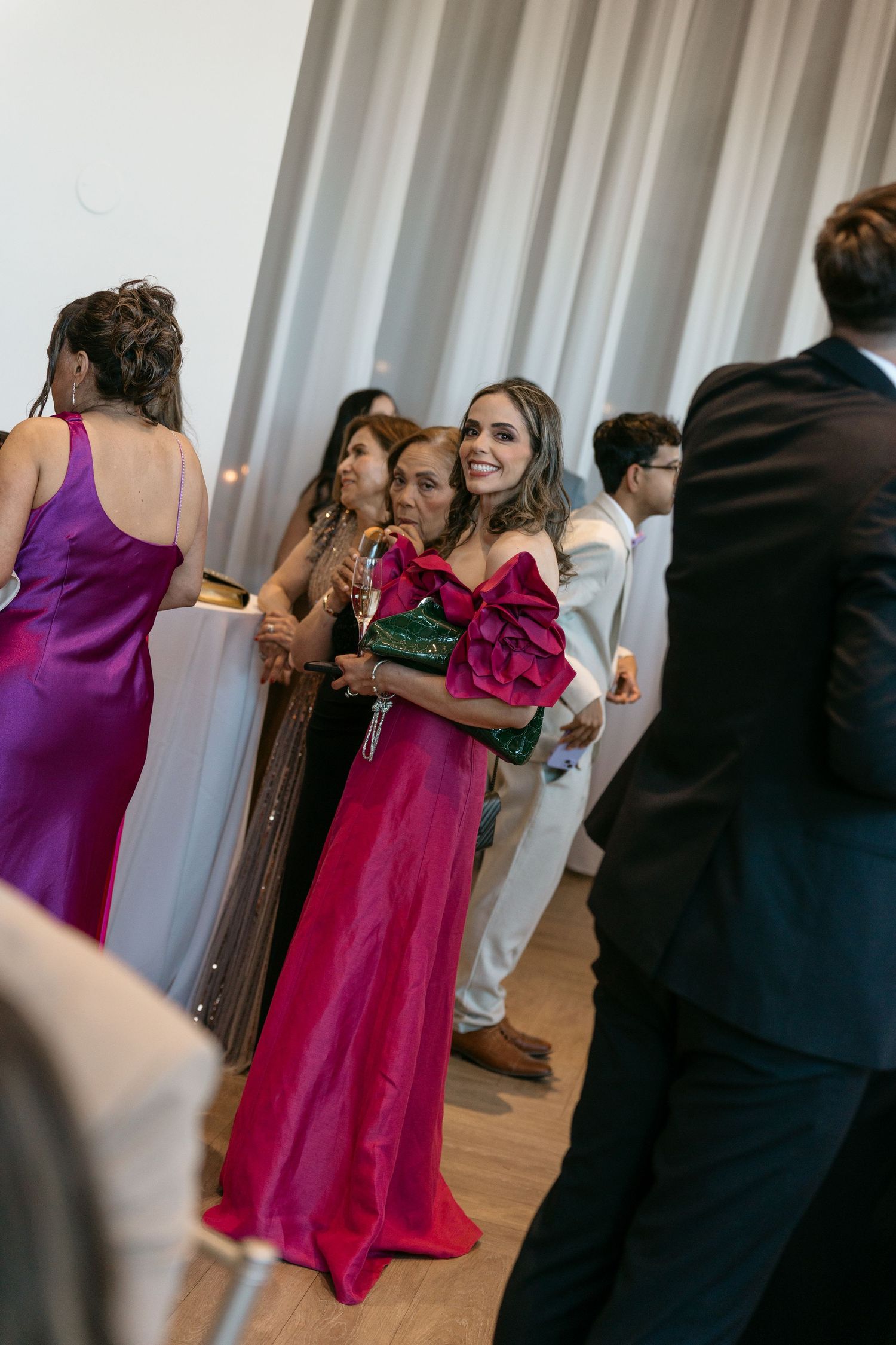 Elegantly dressed wedding guests in colorful gowns mingle at an indoor reception.
