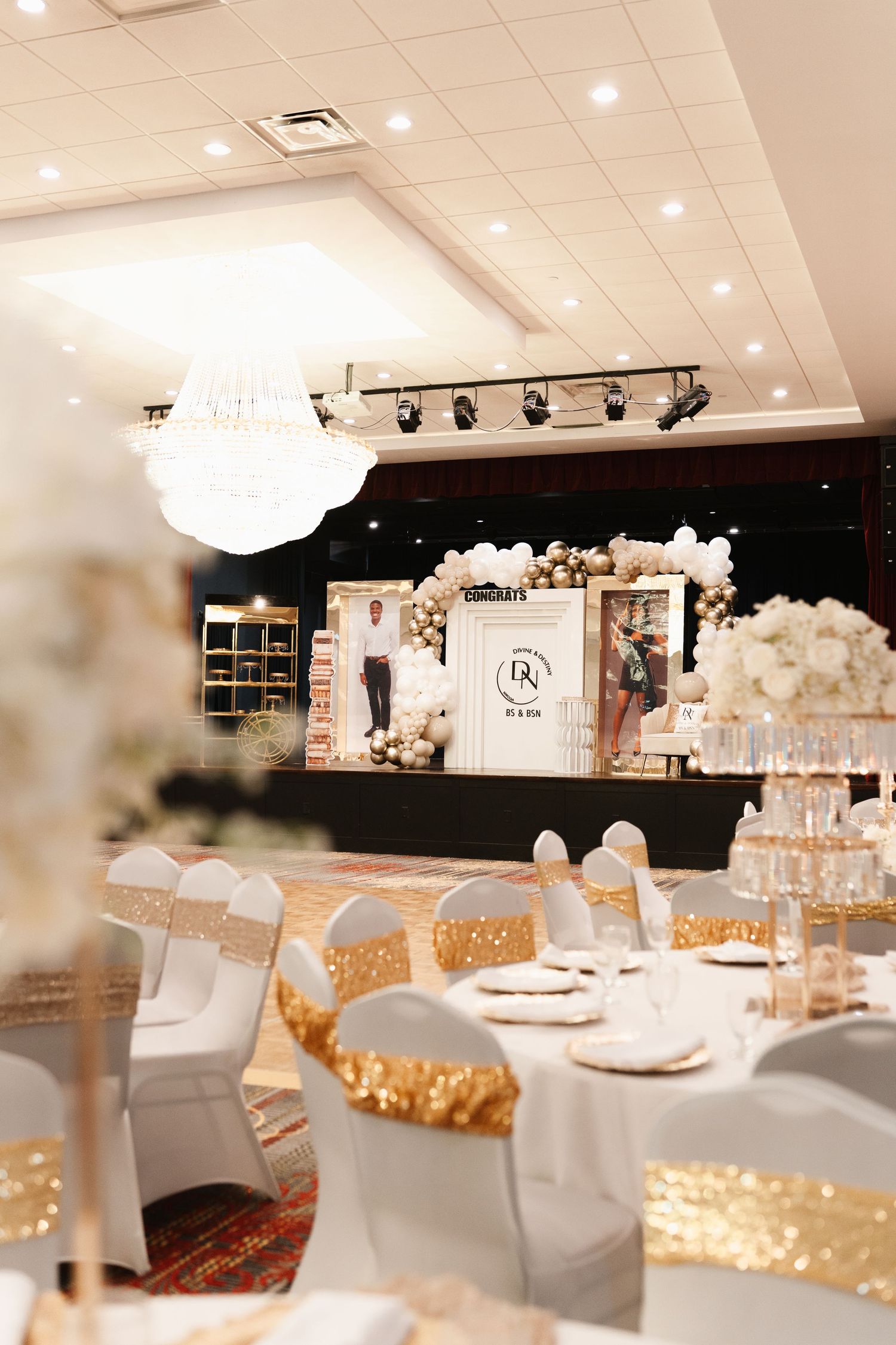 An elegant wedding reception venue with crystal chandelier and white chair covers with gold accents.