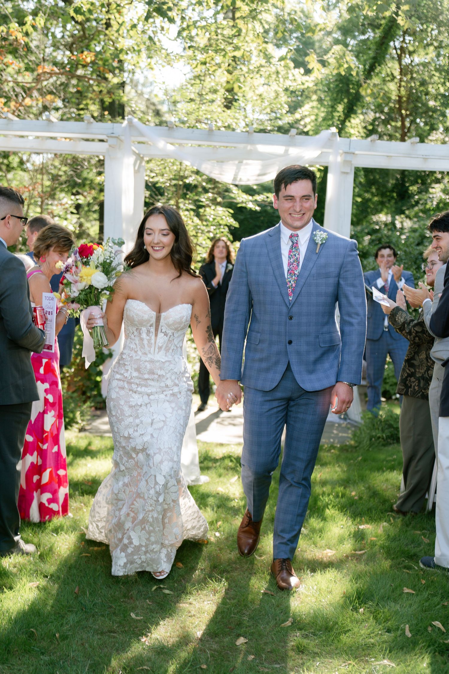 Wedding party walking across a sunny garden lawn during an outdoor ceremony.