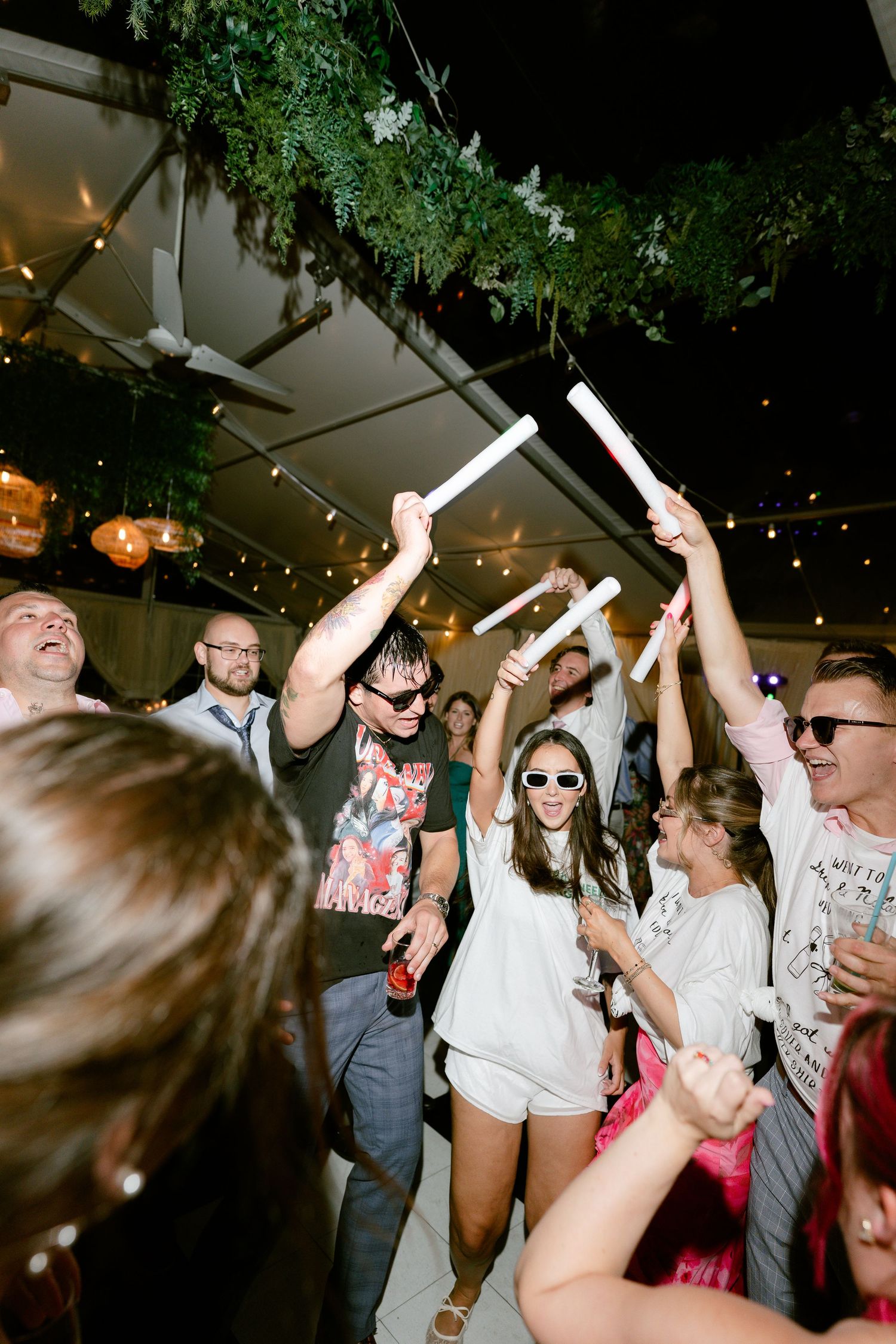 Wedding party dancing and celebrating with streamers under string lights at night.