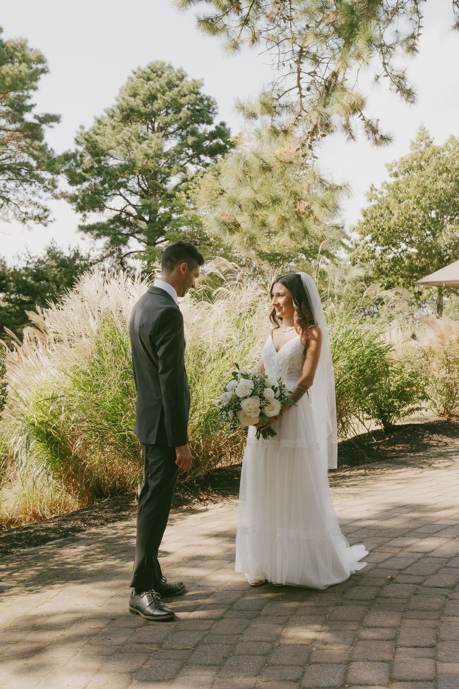 Couple shares intimate first look moment on stone path surrounded by lush greenery and trees.
