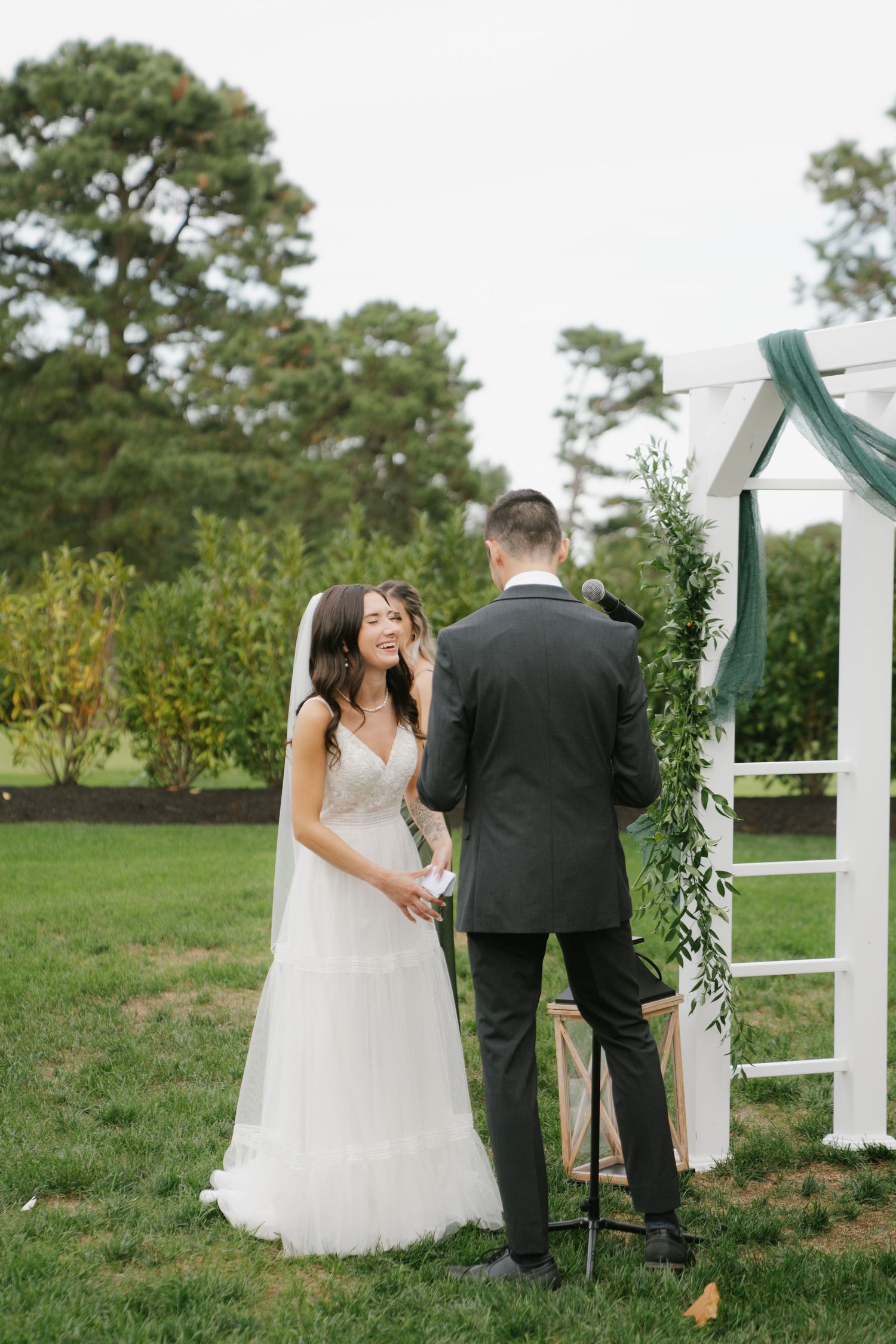 A couple shares a tender moment during their outdoor wedding ceremony near a white arbor in a grassy field.