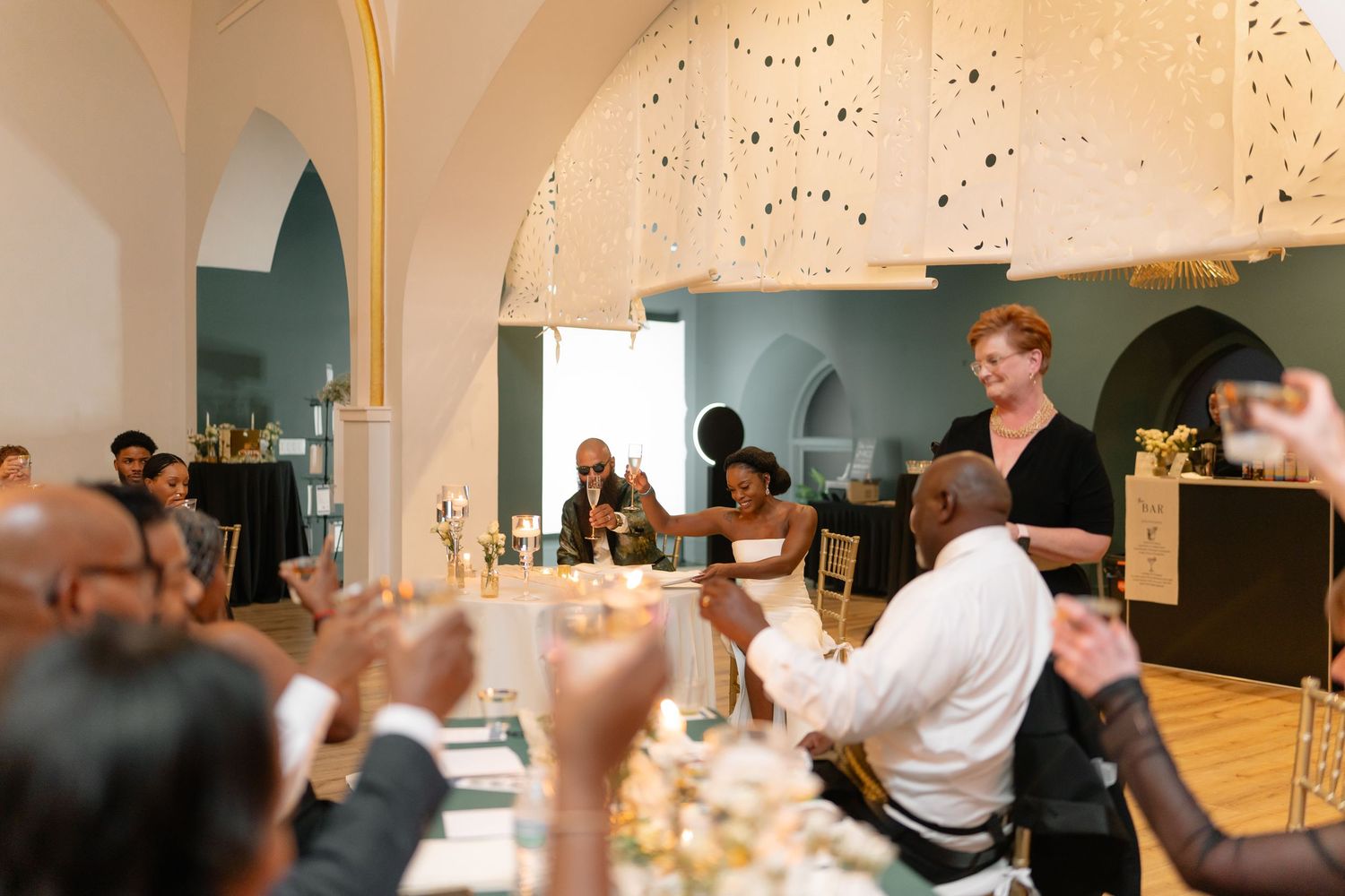 Guests celebrate at a wedding reception in an elegant venue with arched ceilings and mood lighting.
