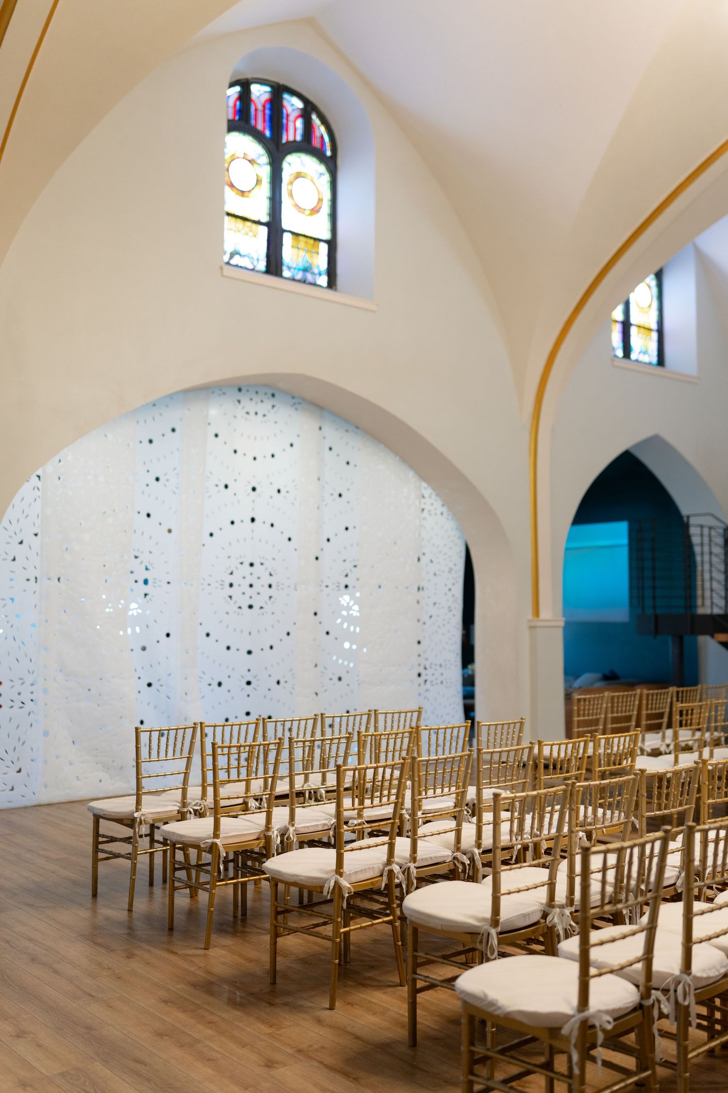 Chapel interior with gold chiavari chairs and stained glass windows in an elegant white arch setting.