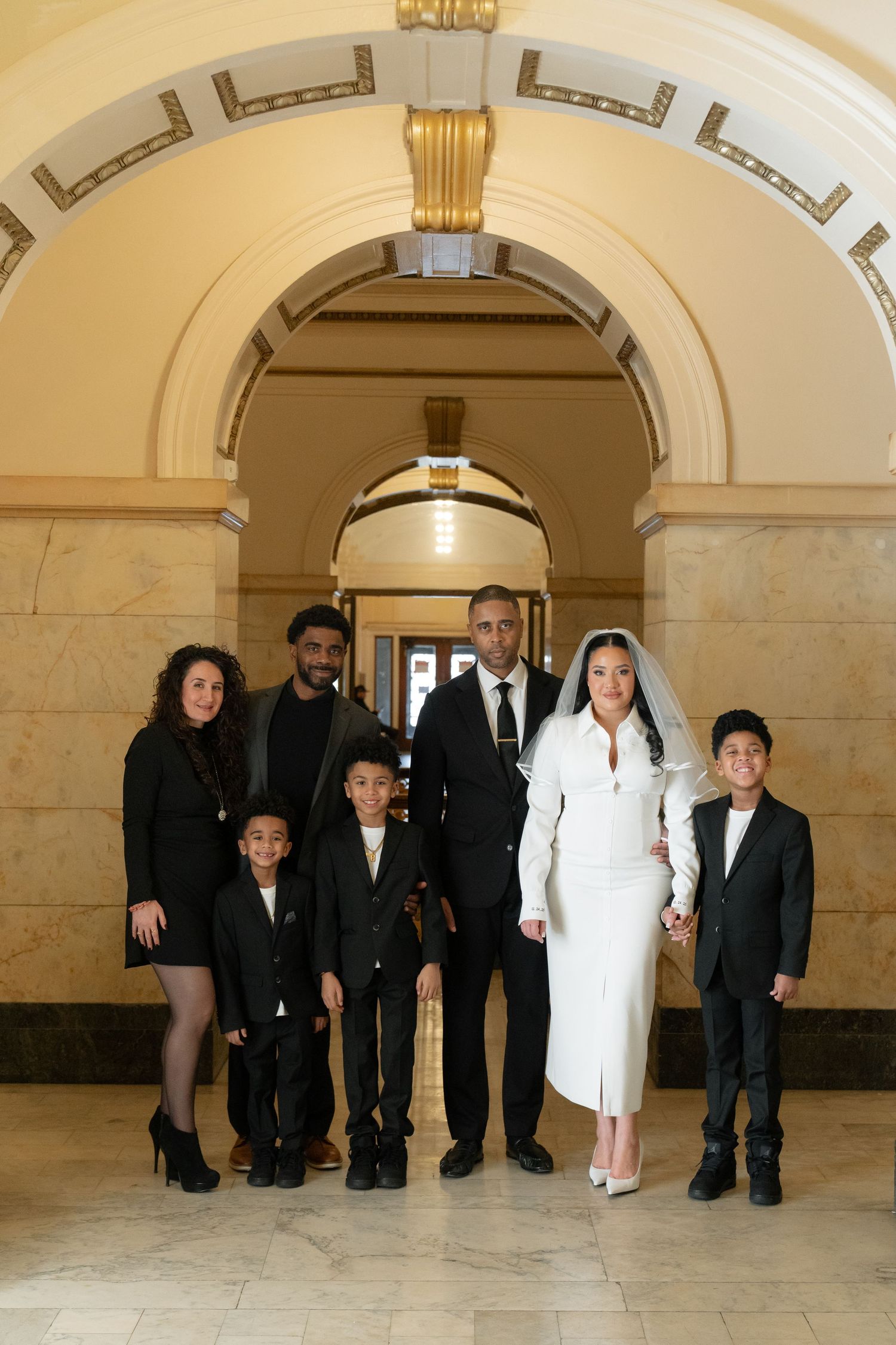 Group photo in formal attire standing under an ornate arched hallway.