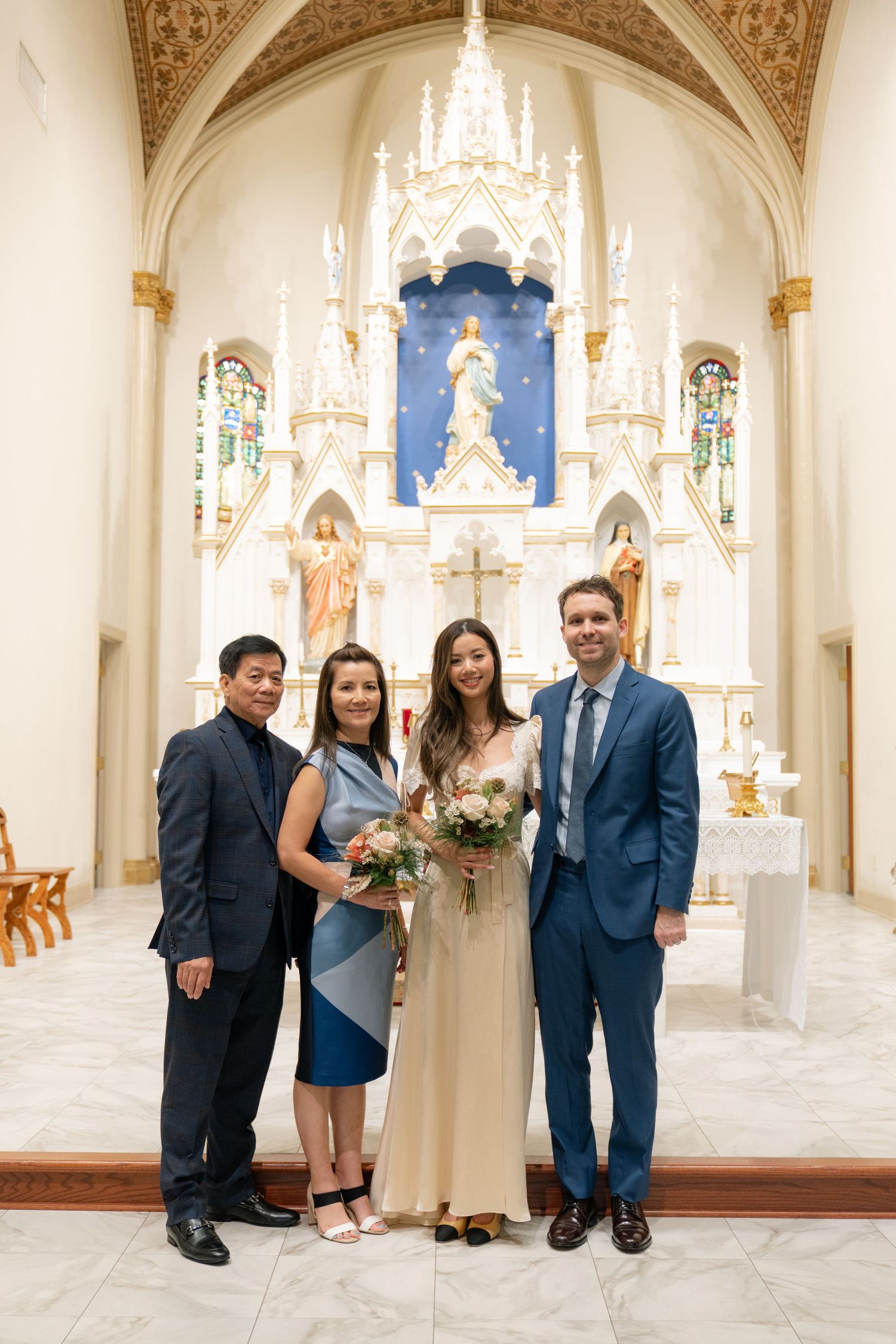 Wedding group photo in front of an ornate white church altar with gothic architecture.