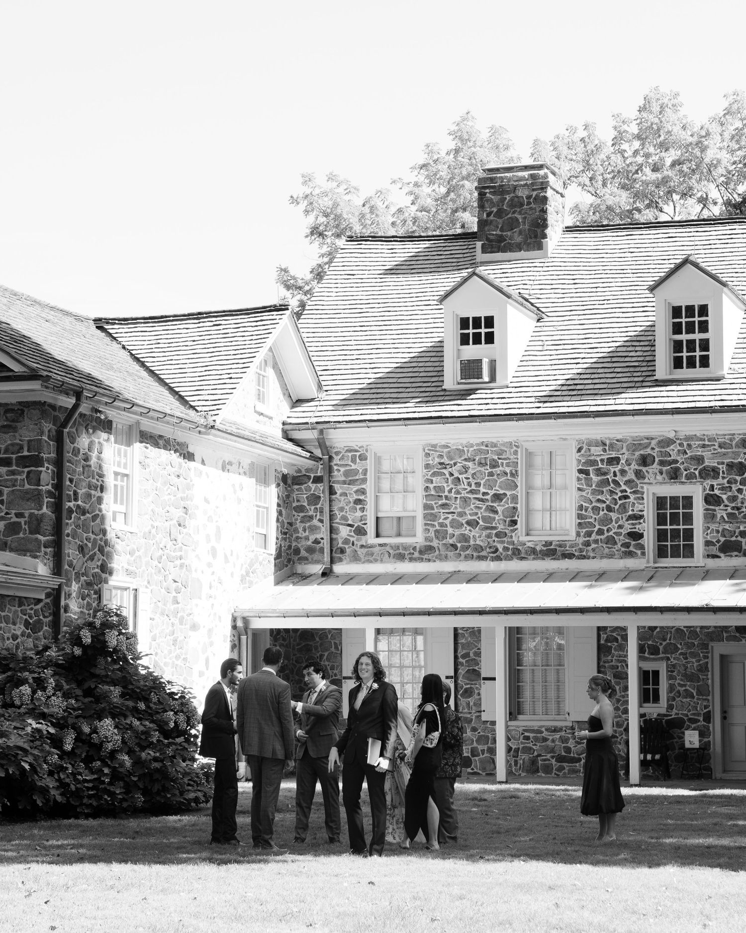 Black and white photo of wedding guests gathered outside a historic stone building.