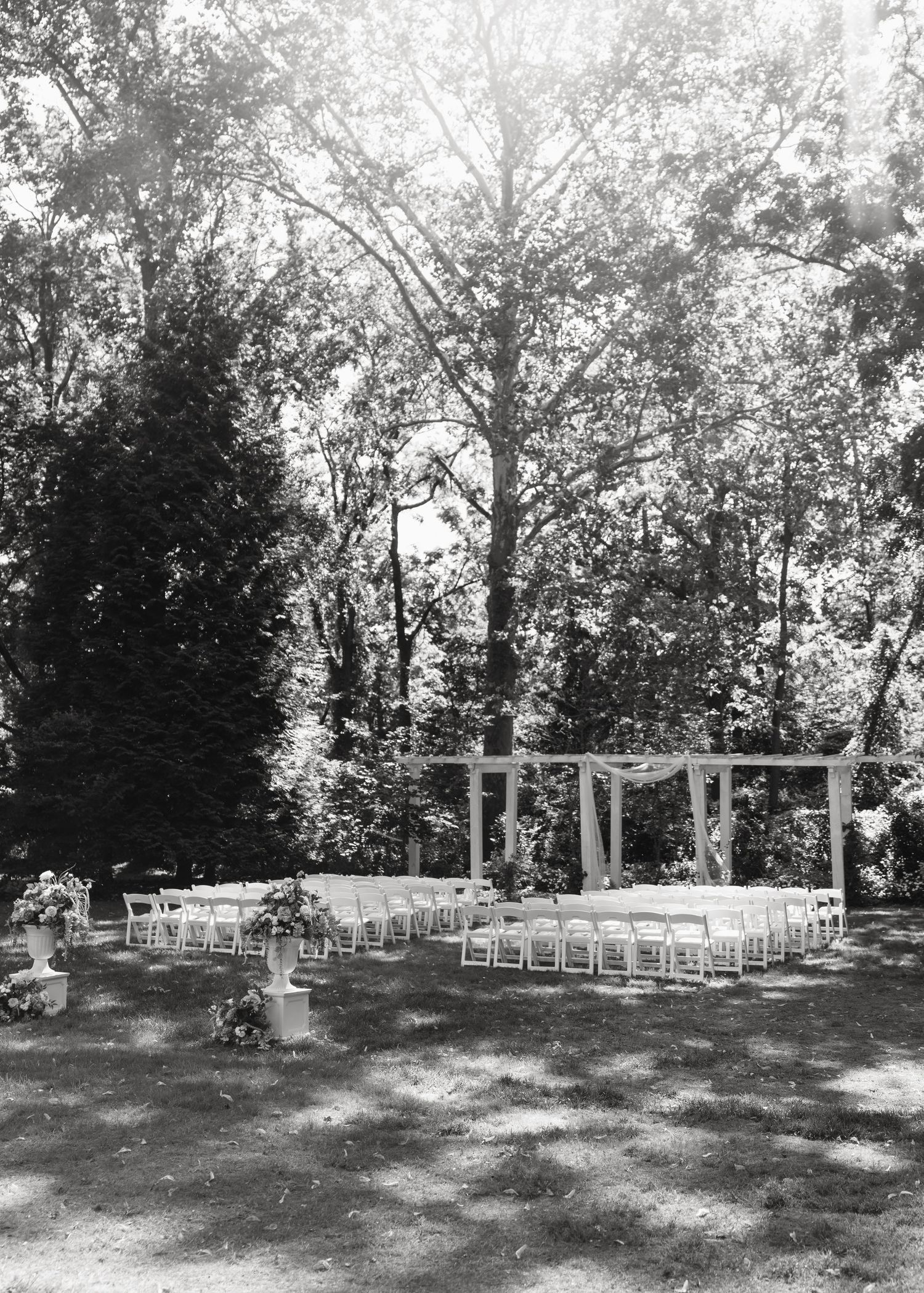 White folding chairs arranged in rows for an outdoor wedding ceremony in a shaded garden setting.