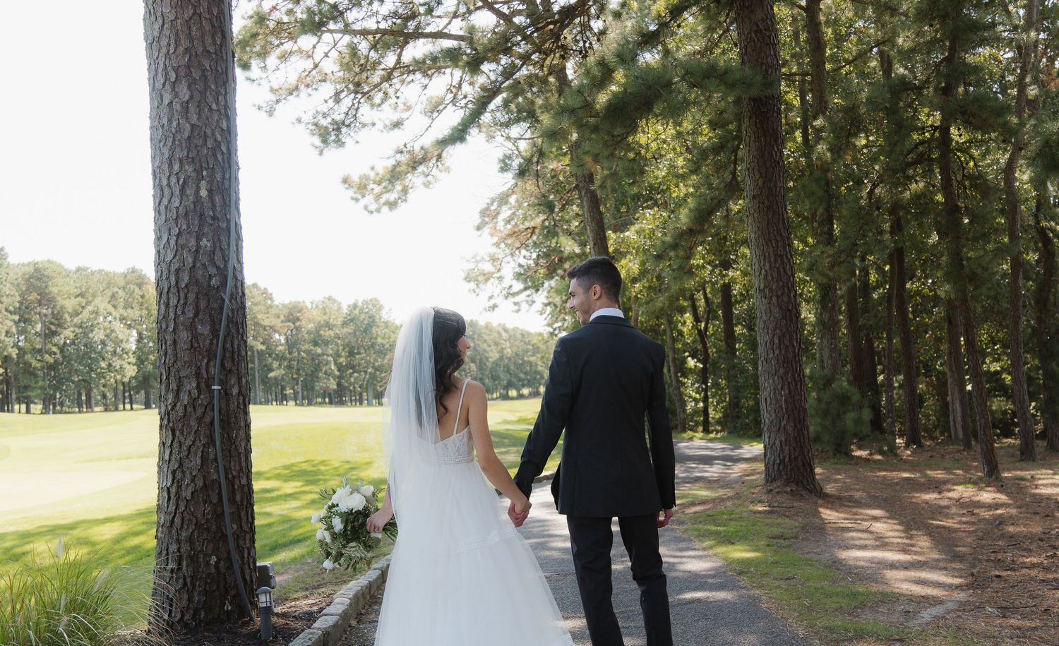 A wedding couple walks hand in hand along a tree-lined path on their special day.