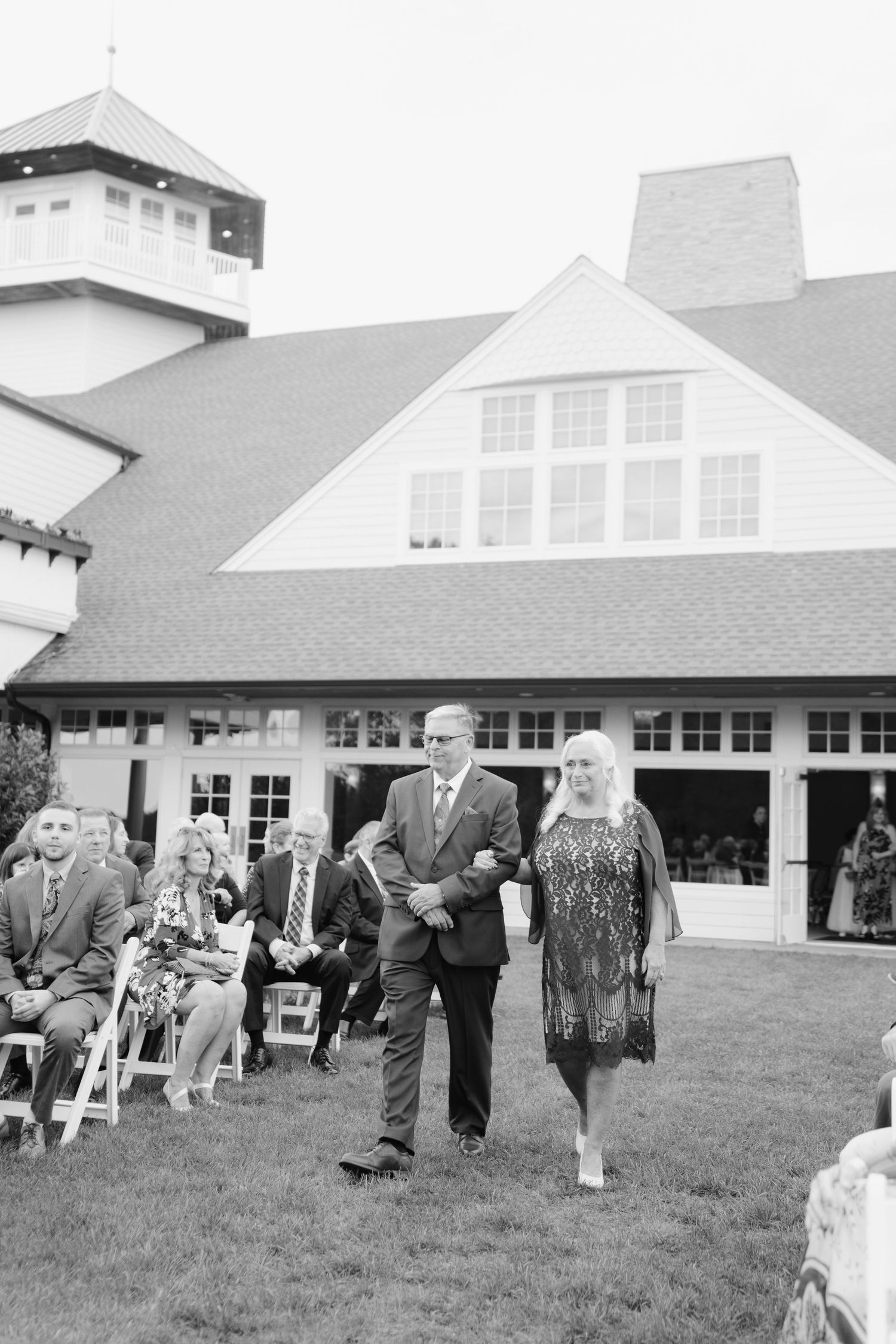 Black and white photo of guests mingling outdoors at a wedding reception near a white building.