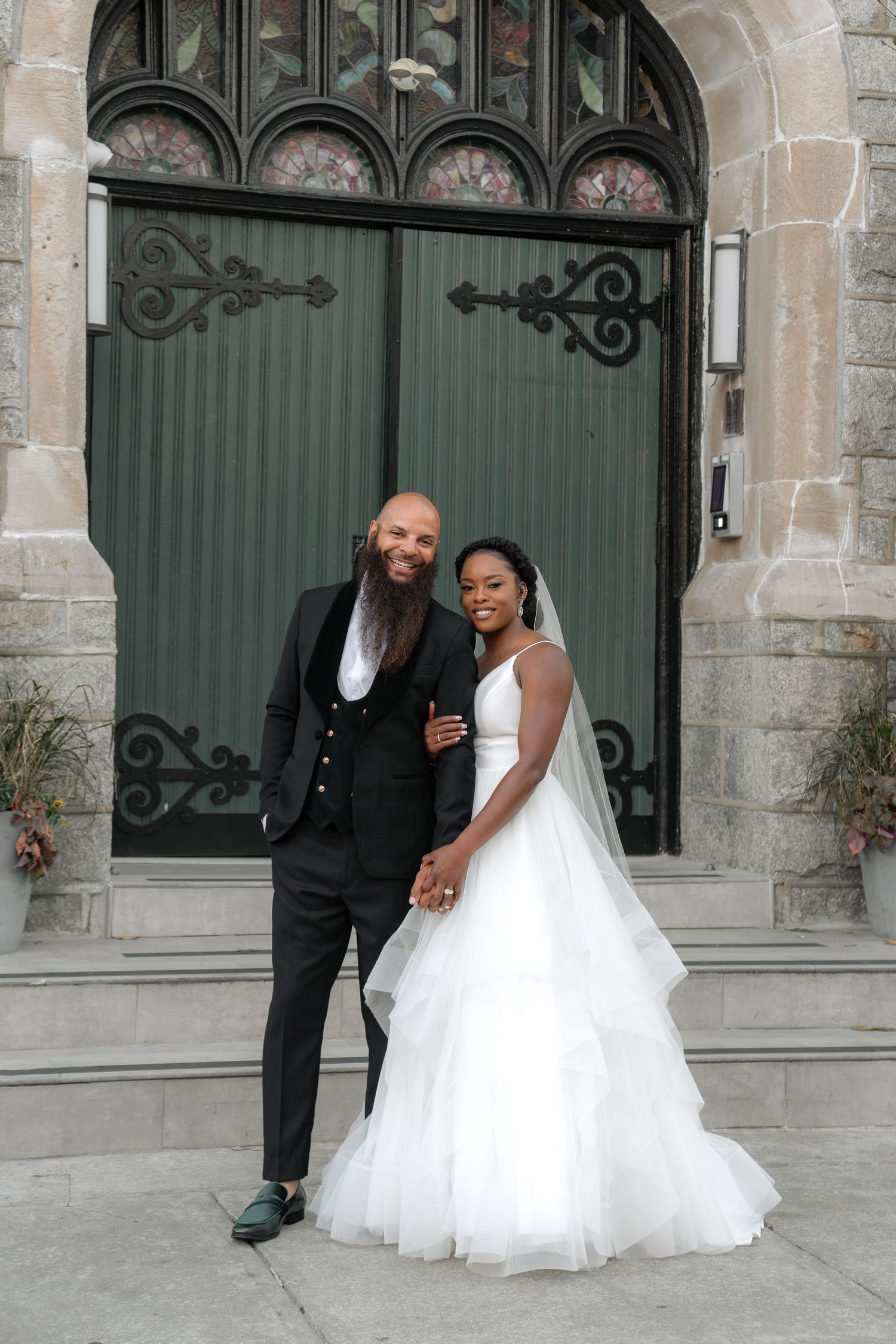 A wedding couple poses for photos in front of an ornate stone church entrance.