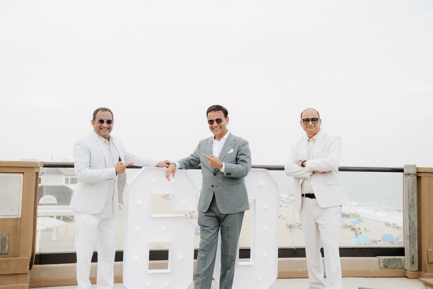 Wedding party in white and grey attire poses against bright outdoor backdrop.