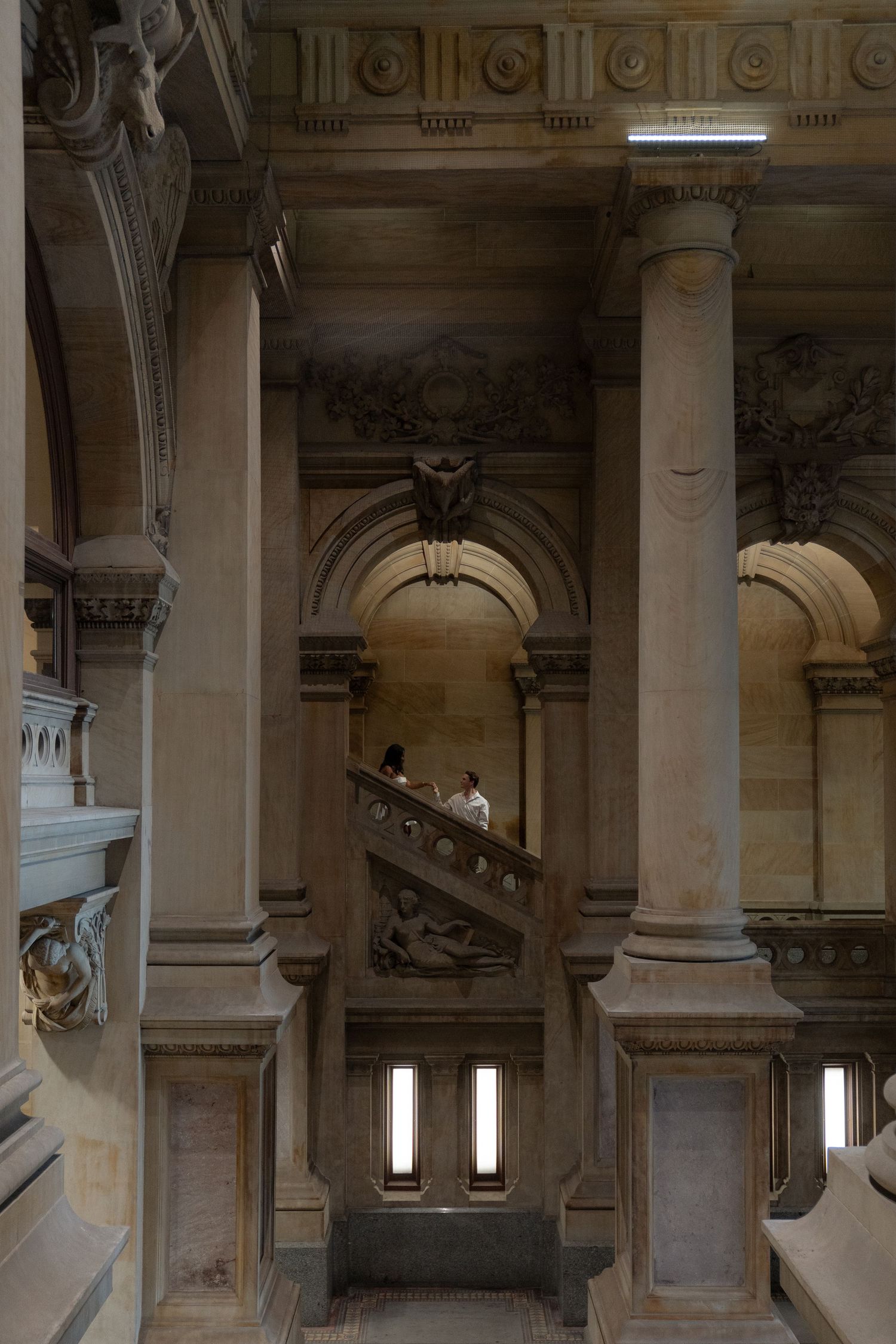 Classical stone interior with grand columns and arched staircase in a historic building with dramatic lighting.