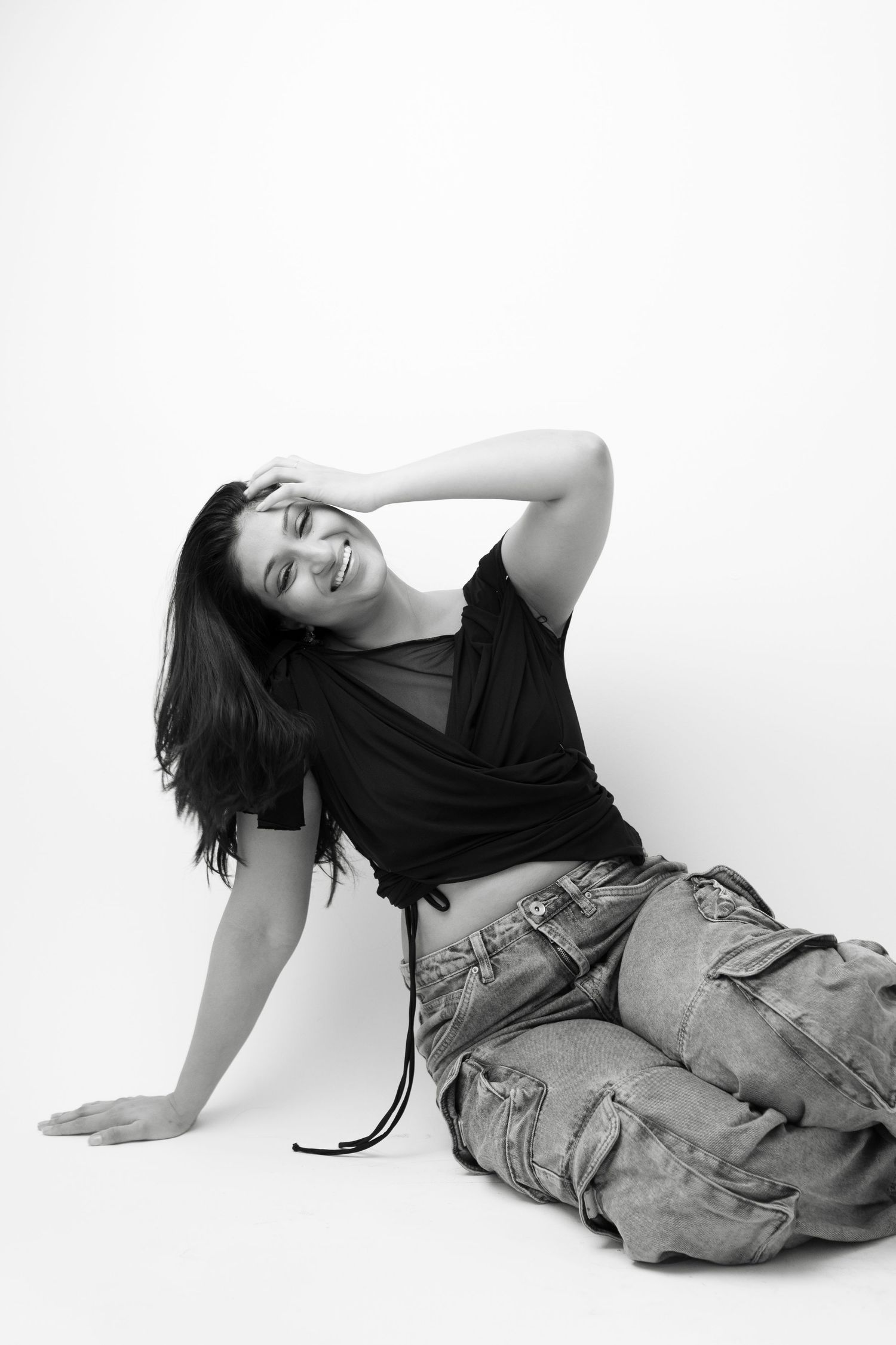 A person in casual denim clothing lies on a white background in an artistic black and white photoshoot.