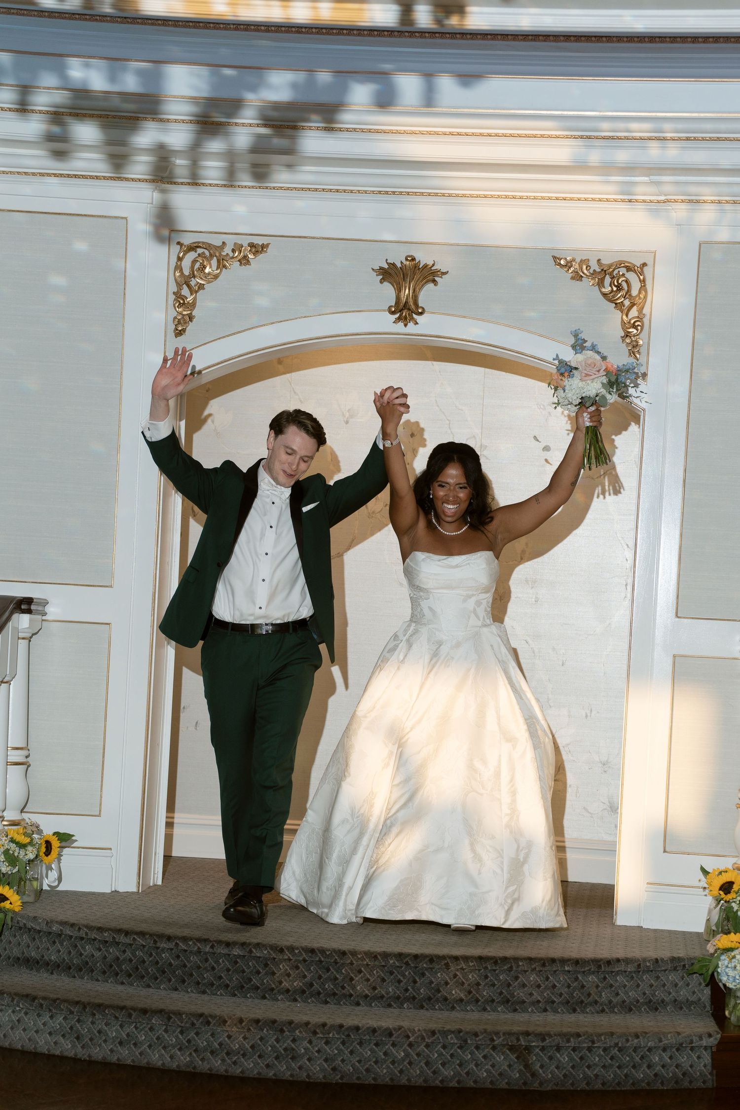 Joyful newlywed interracial couple raises hands in celebration after wedding ceremony at ornate altar.