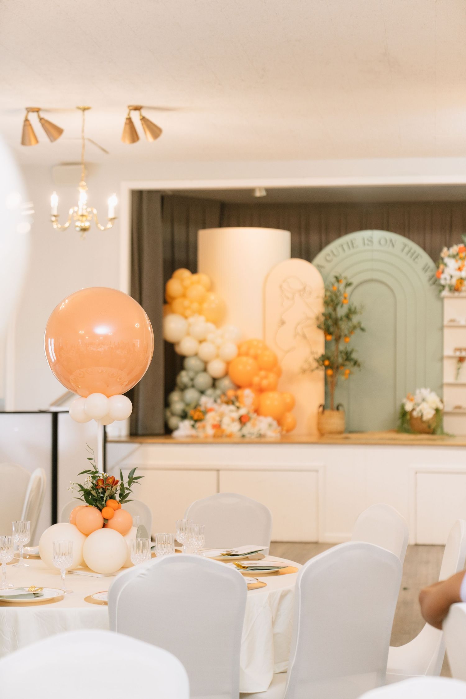 Modern event space with peach balloons, white chairs, and elegant table settings.