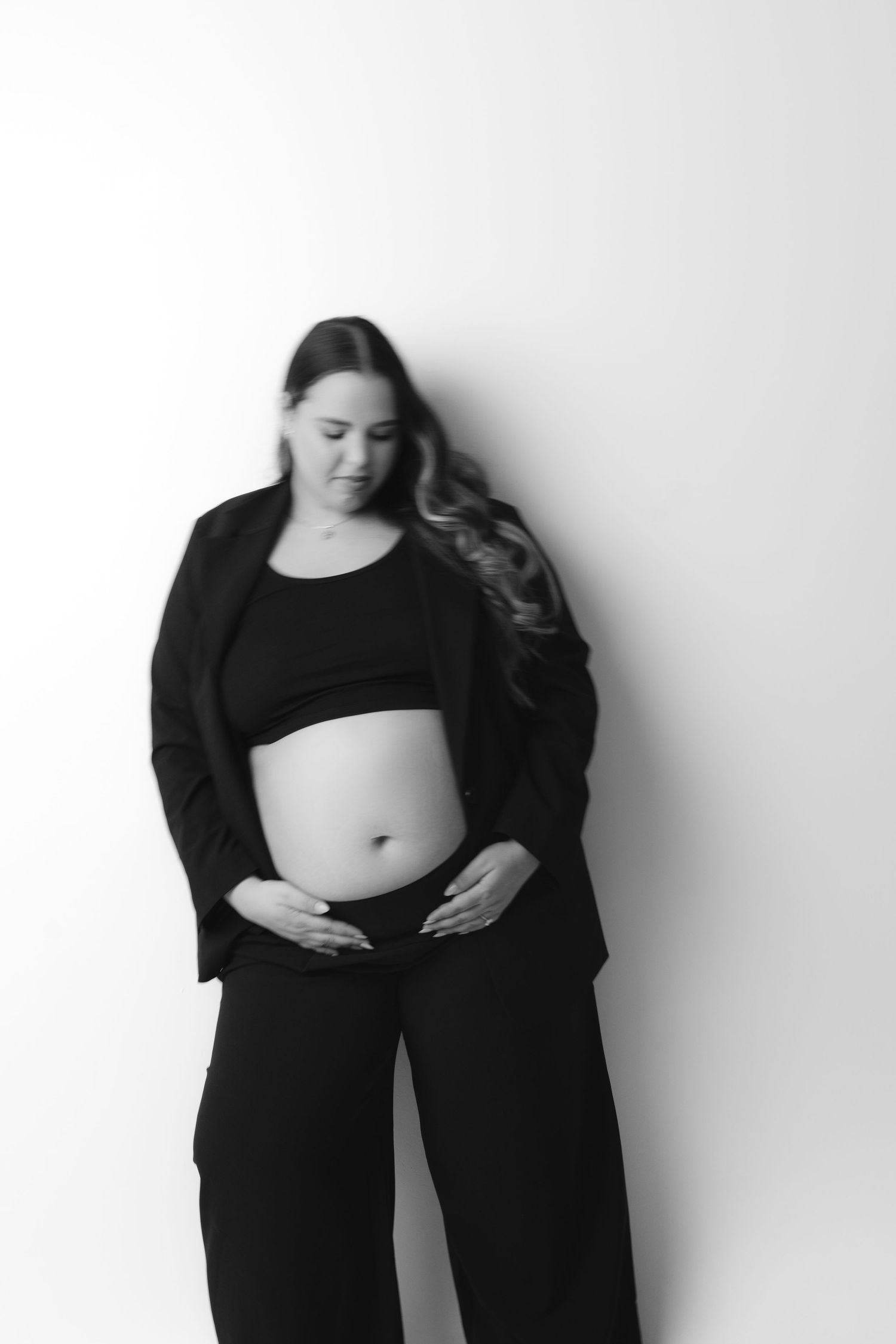 Minimalist black and white maternity photos against plain white backdrop show figure in black attire.