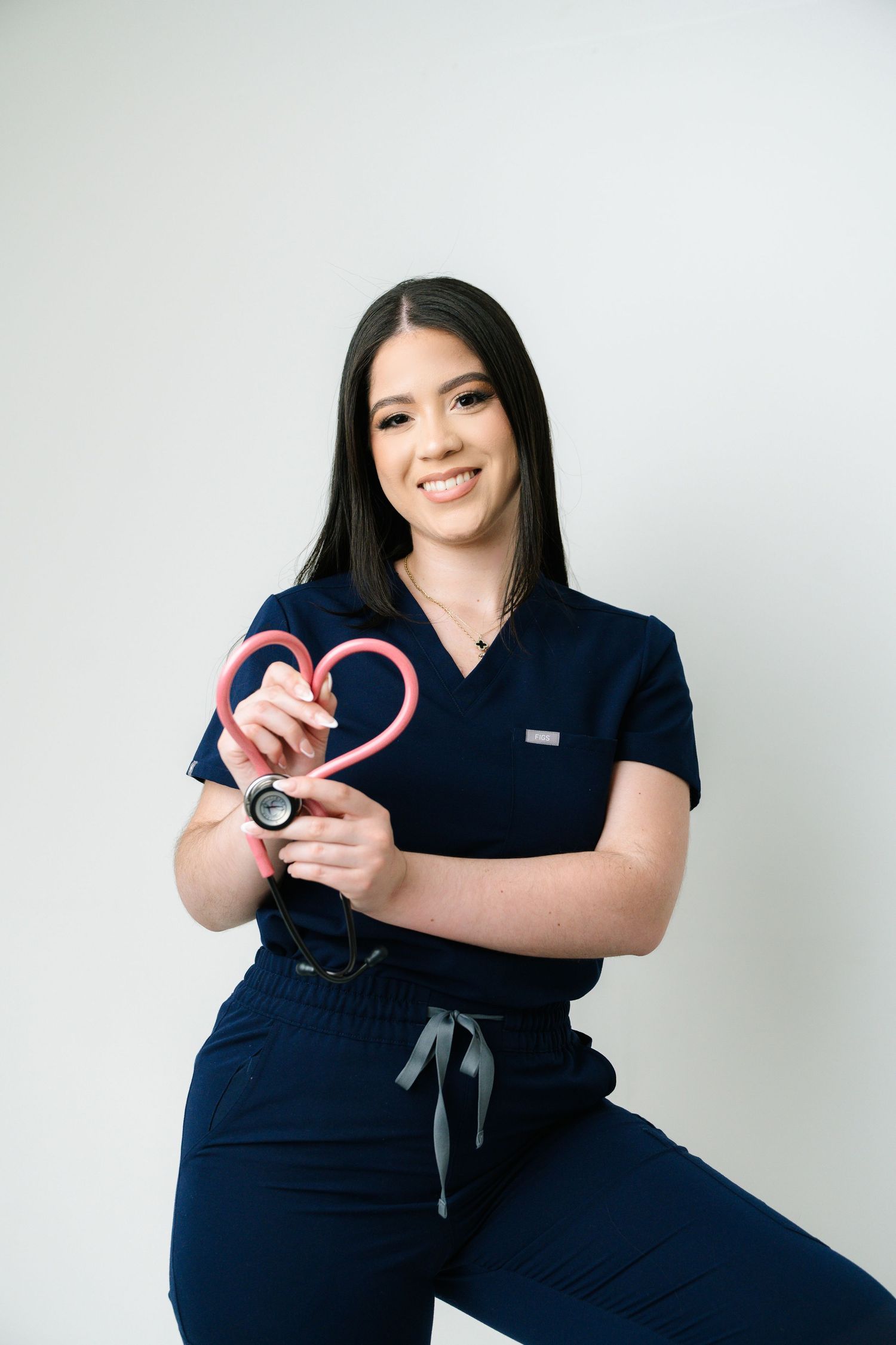 Healthcare worker in navy scrubs poses playfully with medical equipment against white background.