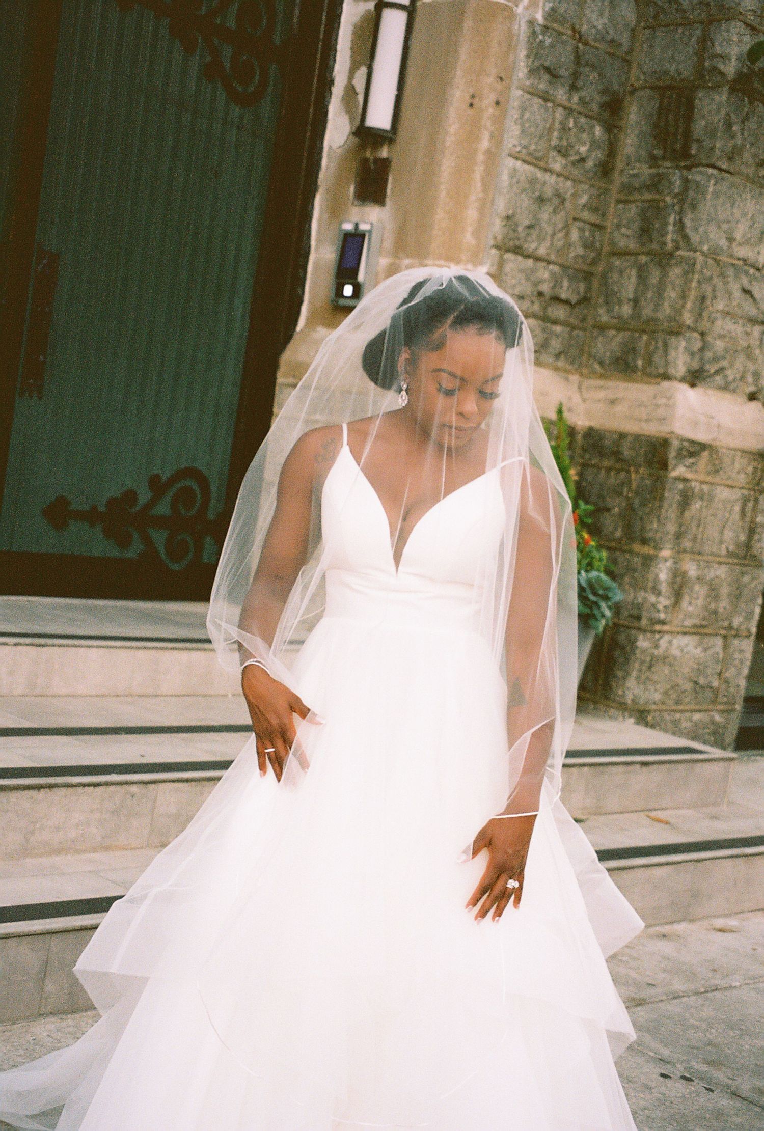Bride in flowing white wedding gown poses outside with dramatic train detail.