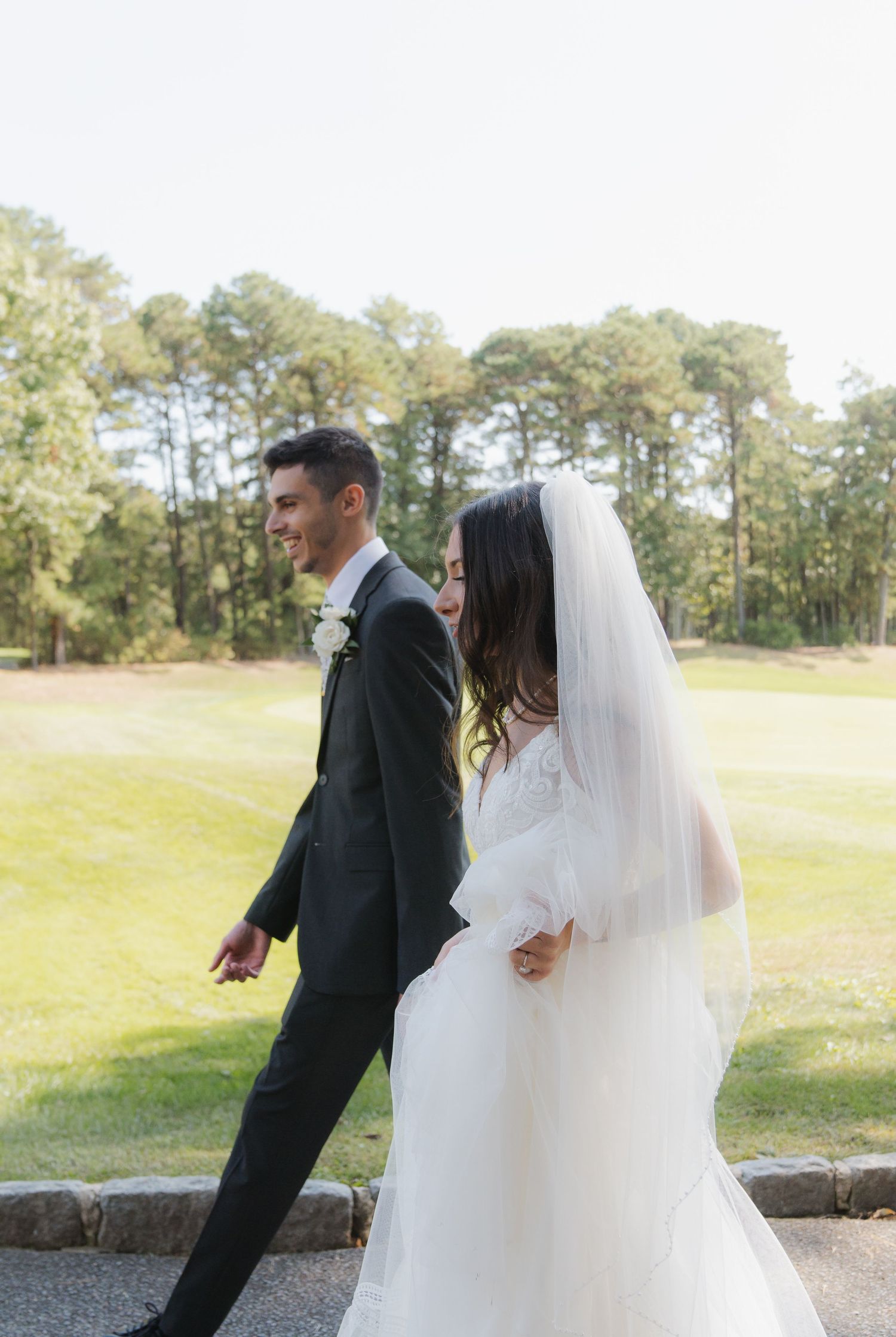 A couple in wedding attire shares a playful moment outdoors with pine trees in the background.