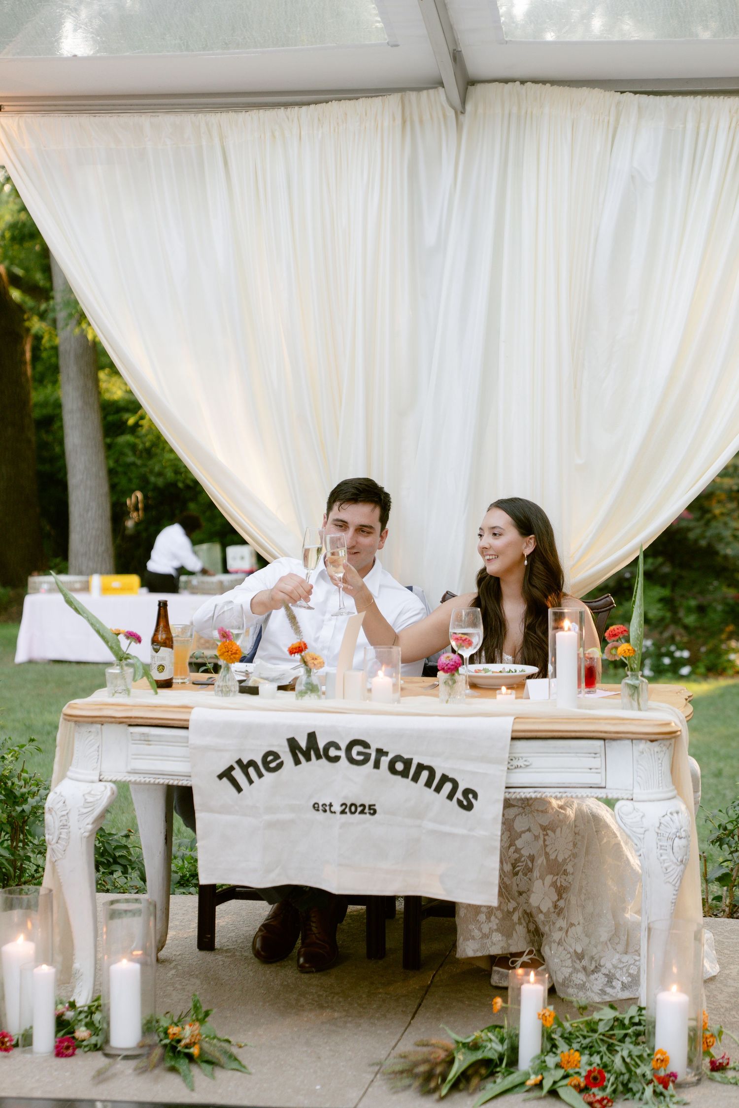 Elegant wedding reception setup with white draping, floral arrangements, and personalized decor.