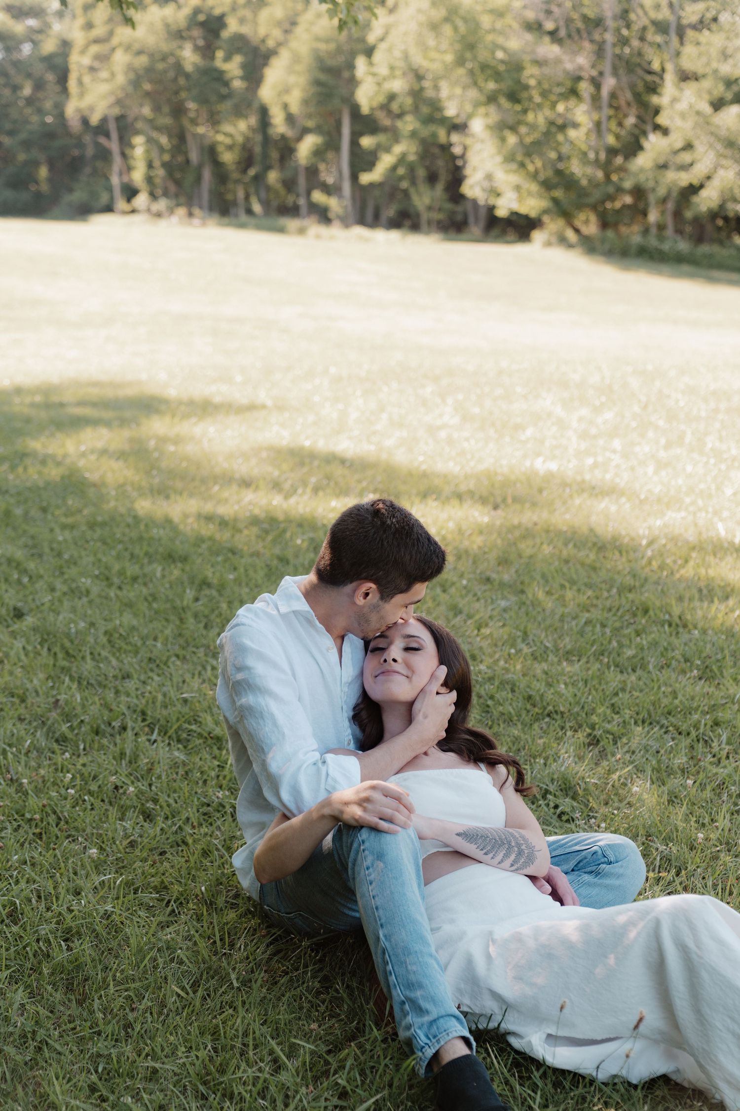 A romantic couple lies in the grass during a tender outdoor moment.