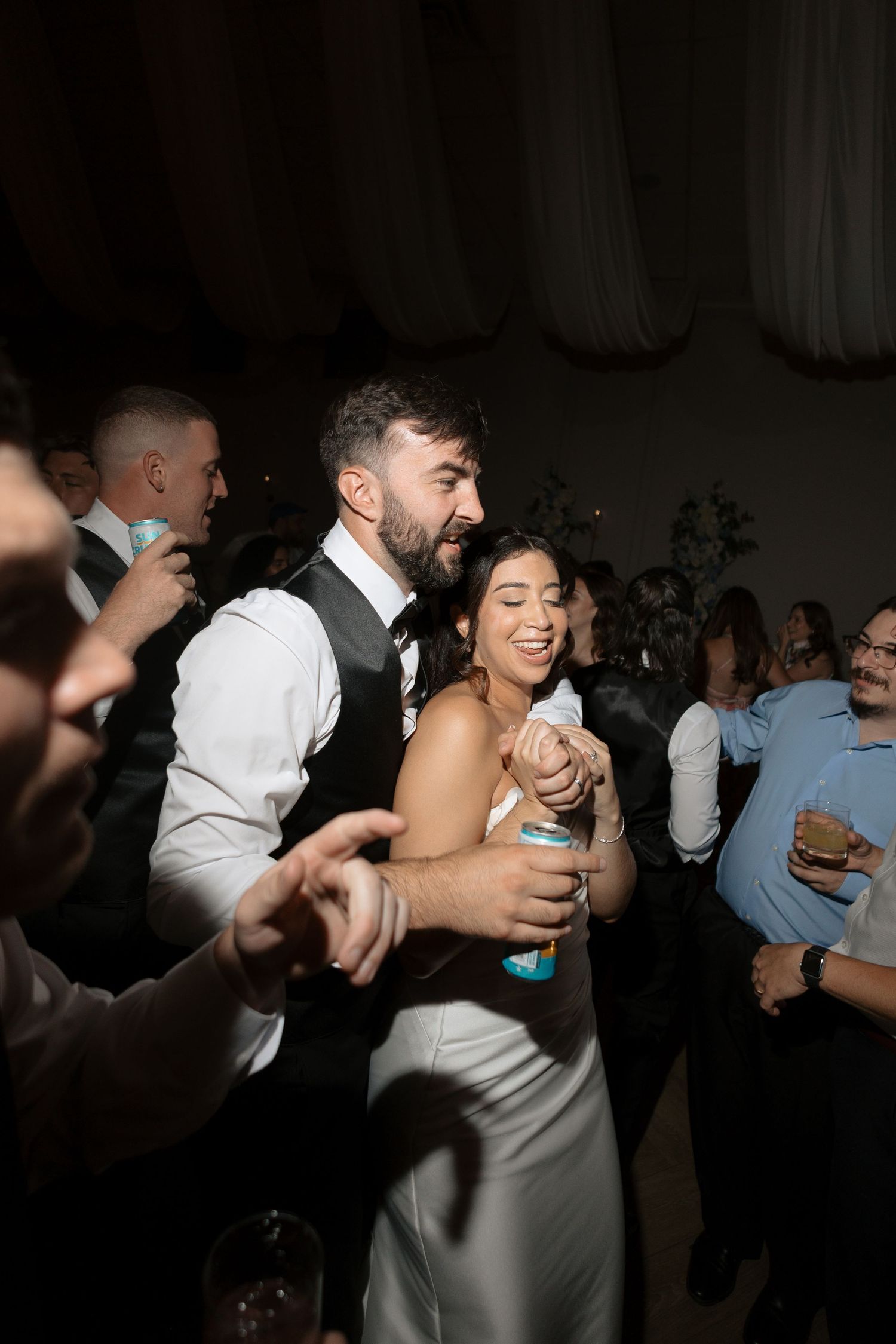 Bride and groom dance joyfully together surrounded by guests at lively wedding reception.