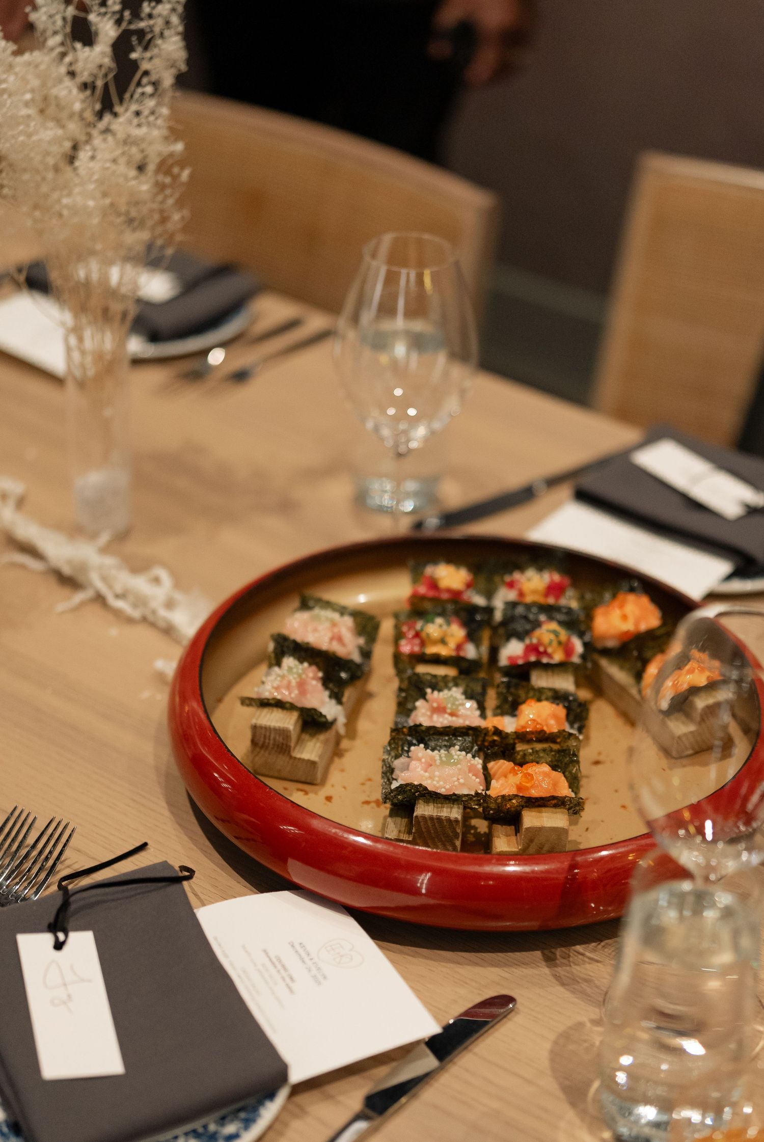 An elegant table setting with sushi plates and wine glasses arranged on a wooden surface.