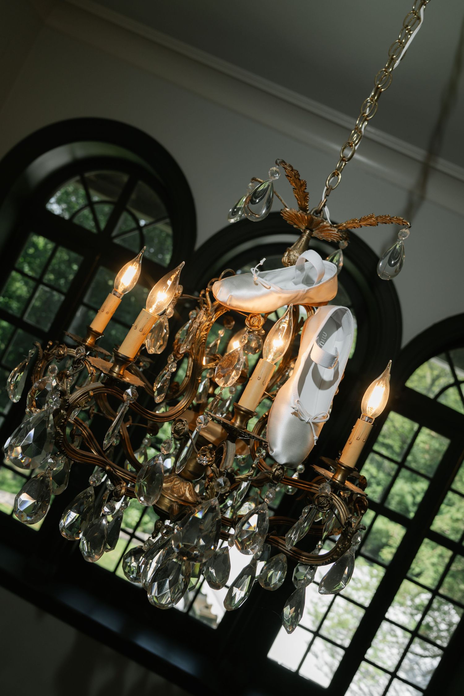 Vintage crystal chandelier with candle-style lights hangs dramatically against arched windows.