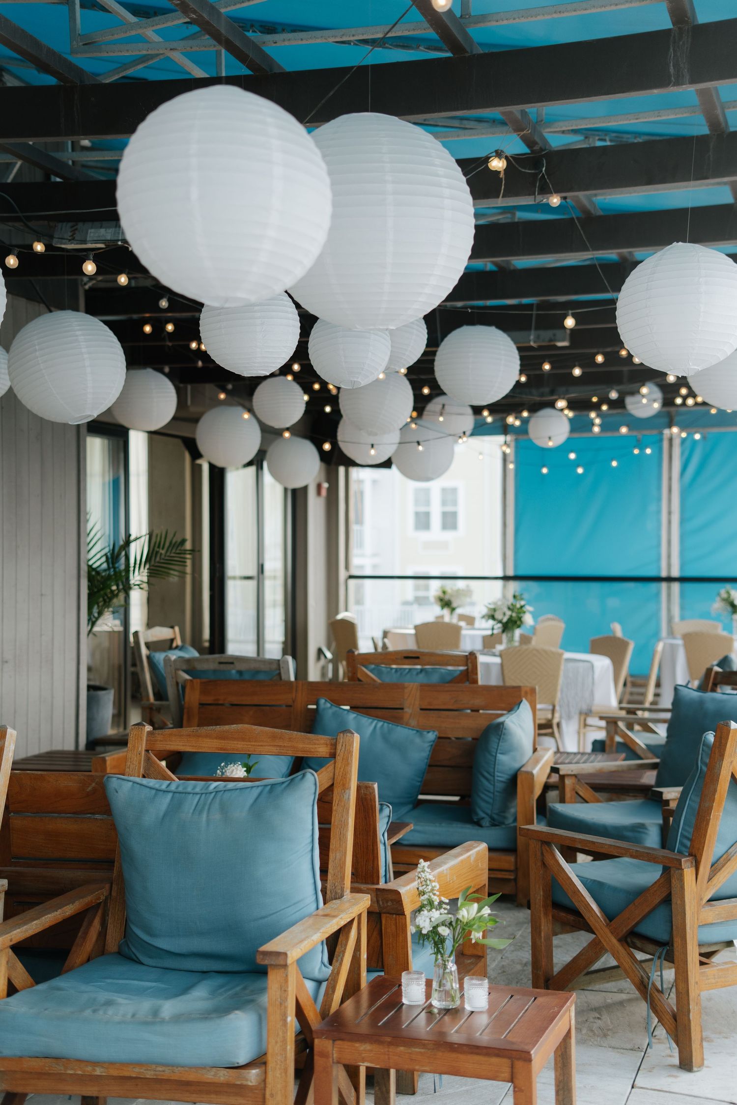 Coastal lounge area with wooden furniture, blue cushions and white paper lanterns.