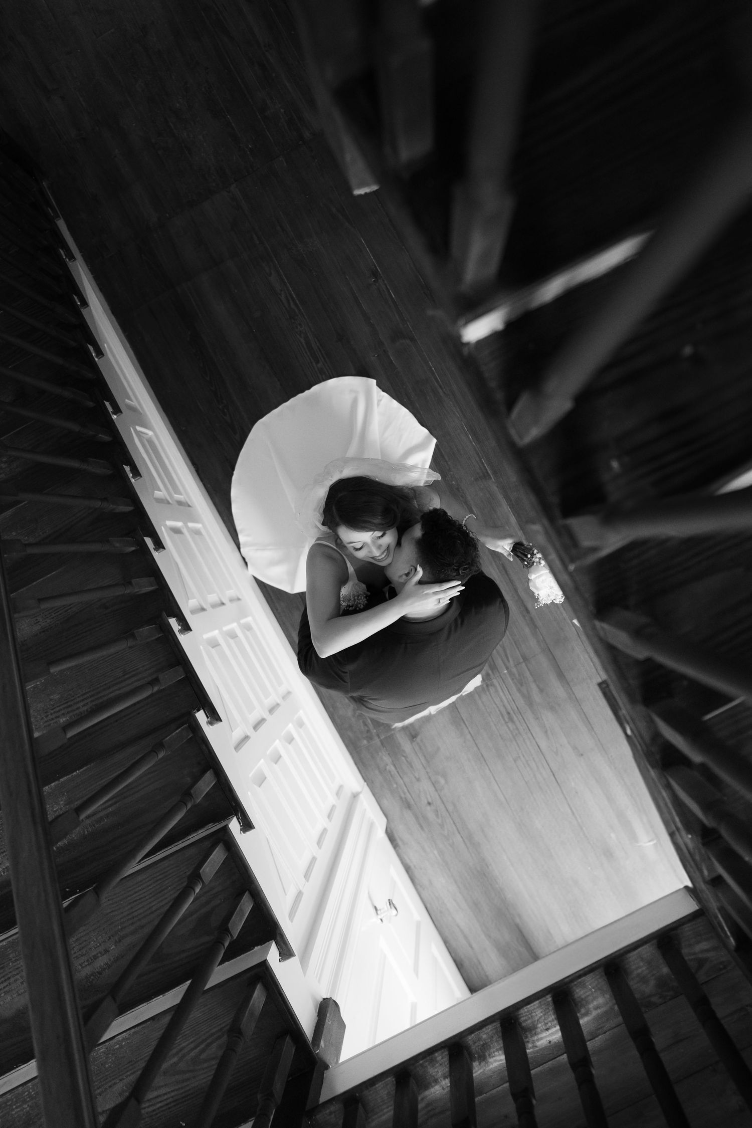 Aerial black and white photo of a person sitting alone at a wooden table, viewed from above a spiral staircase.