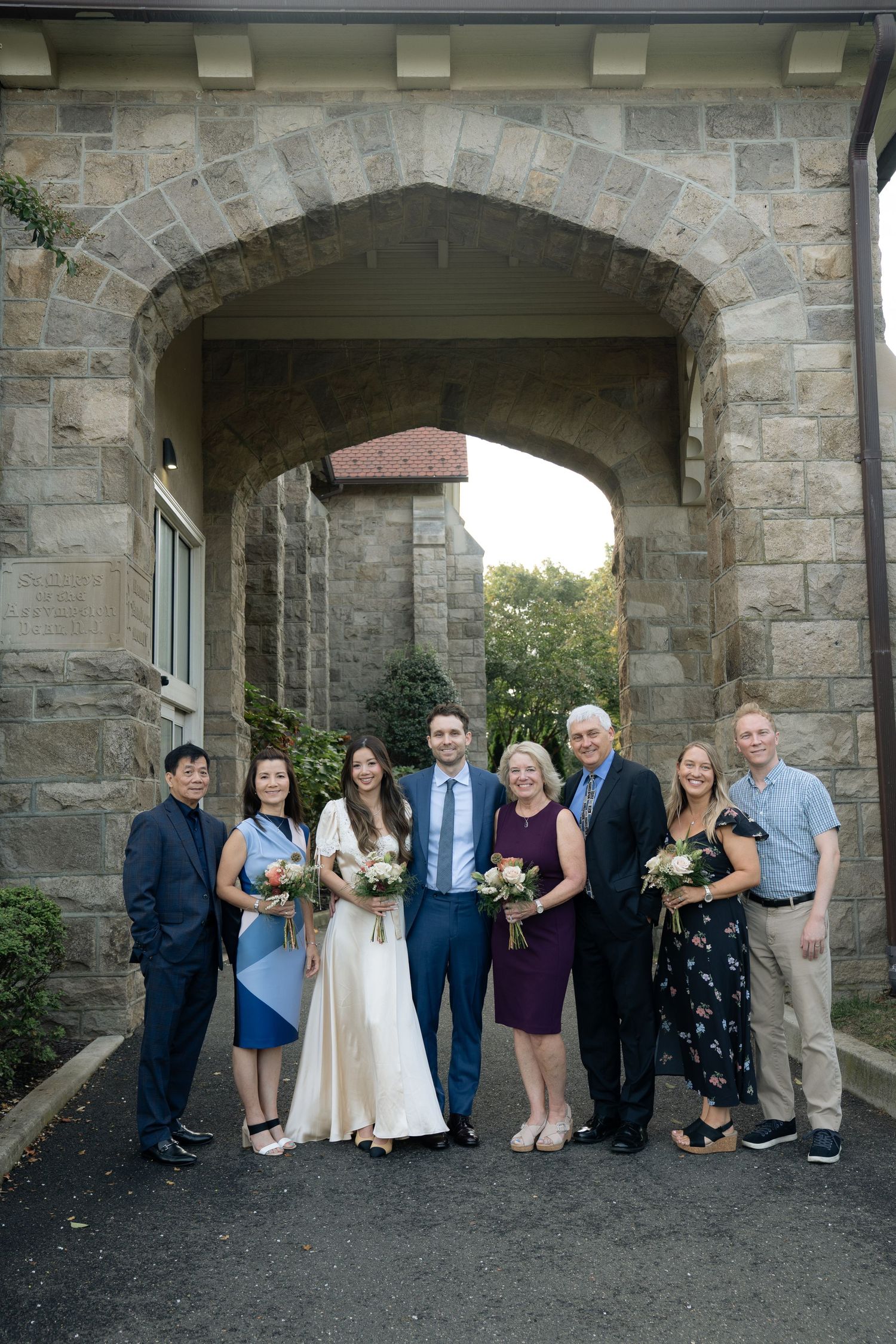 Wedding group photo under stone archway of historic building during autumn.