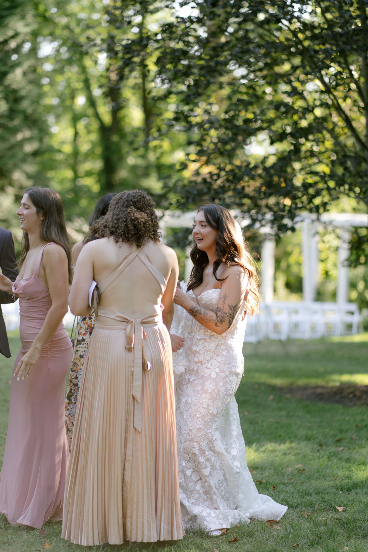 Bridesmaids in blush dresses gather on lawn during outdoor wedding celebration.